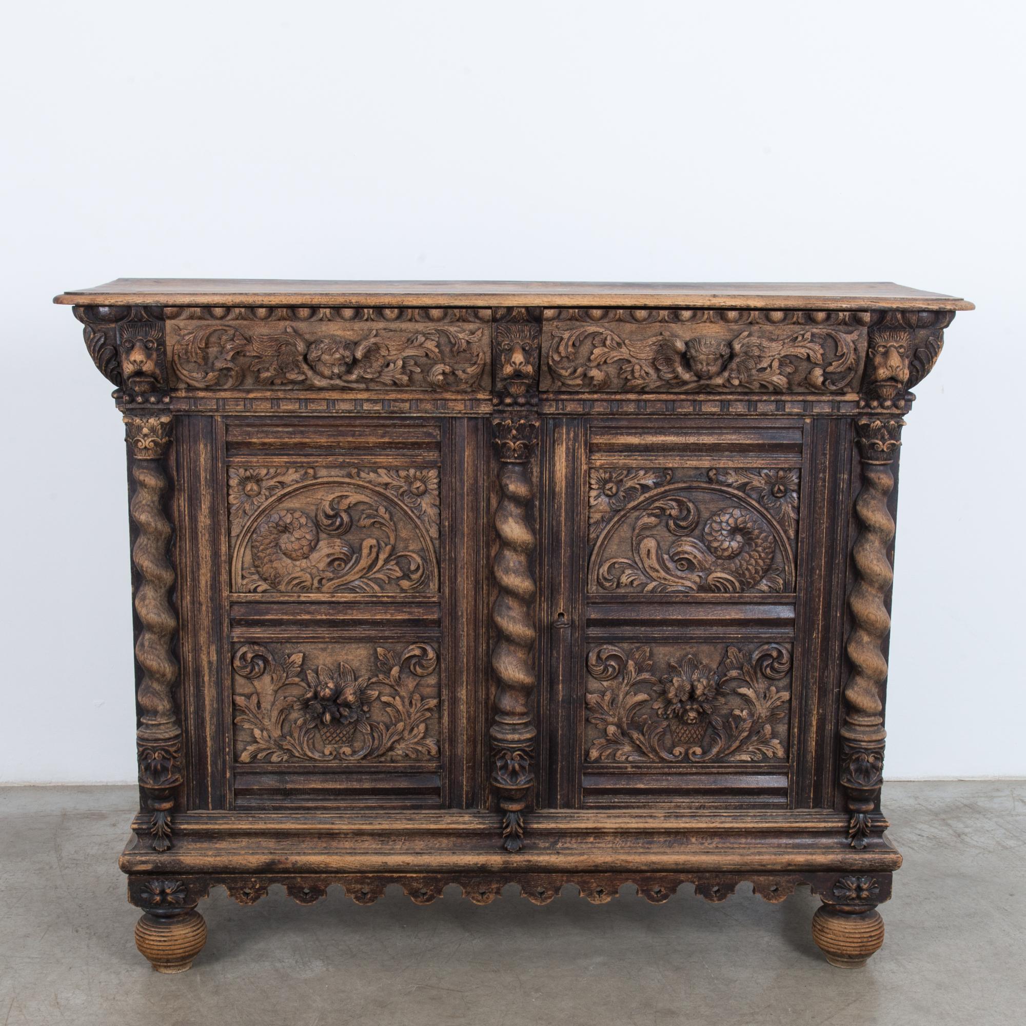 A wooden buffet from Belgium, circa 1820, characterized by ornate carving. Two doors open onto an interior shelf; above are two ample drawers. Ornate Baroque designs embellish every surface of the dark wood. Cherubs, sea monsters, leaves, flowers