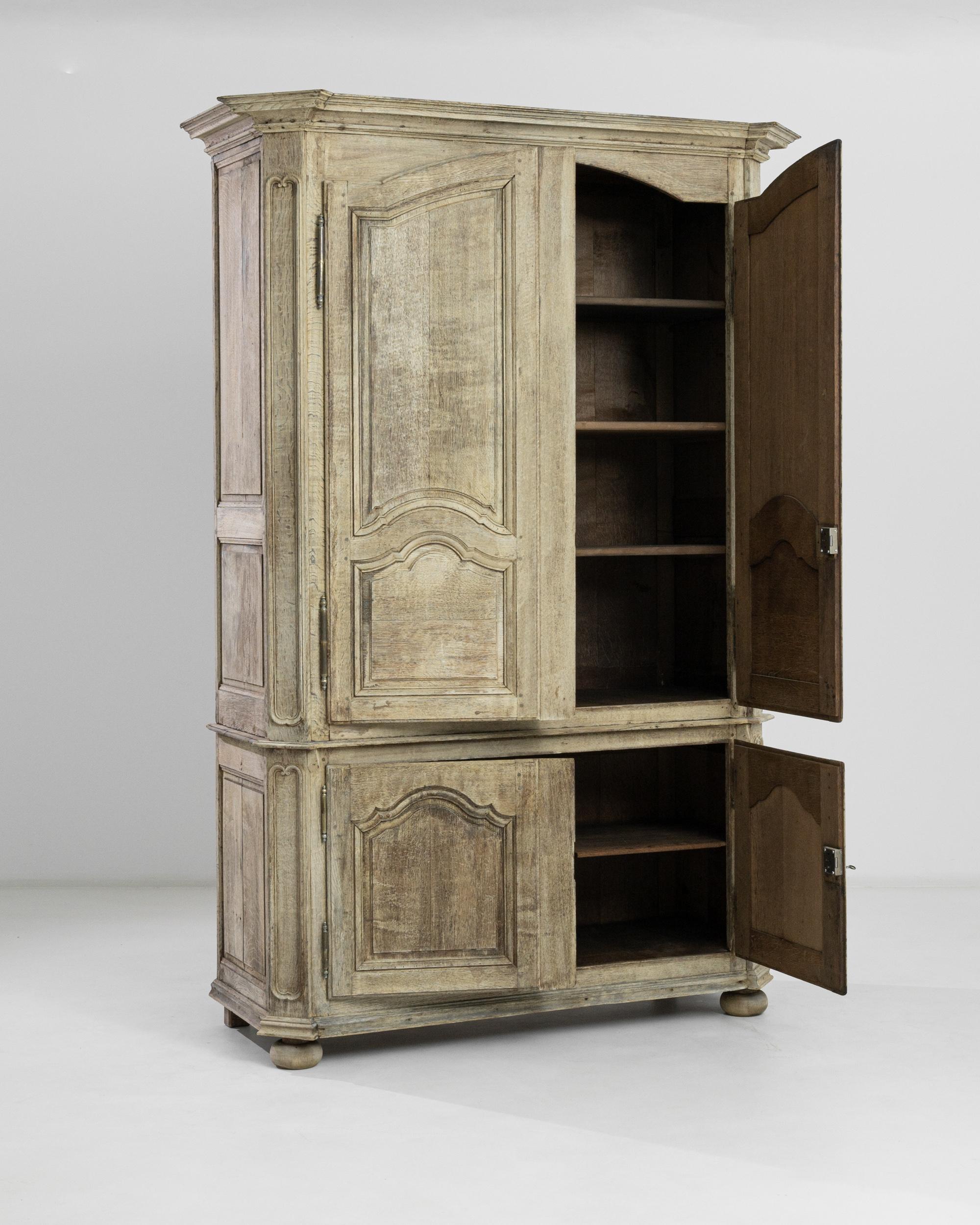This tall armoire was crafted in Belgium, circa 1820. Standing on bun feet, this antique treasure features a carved front, brass scrolled escutcheons and an angled molded crown for an original profile. The doors open to reveal the natural chocolate