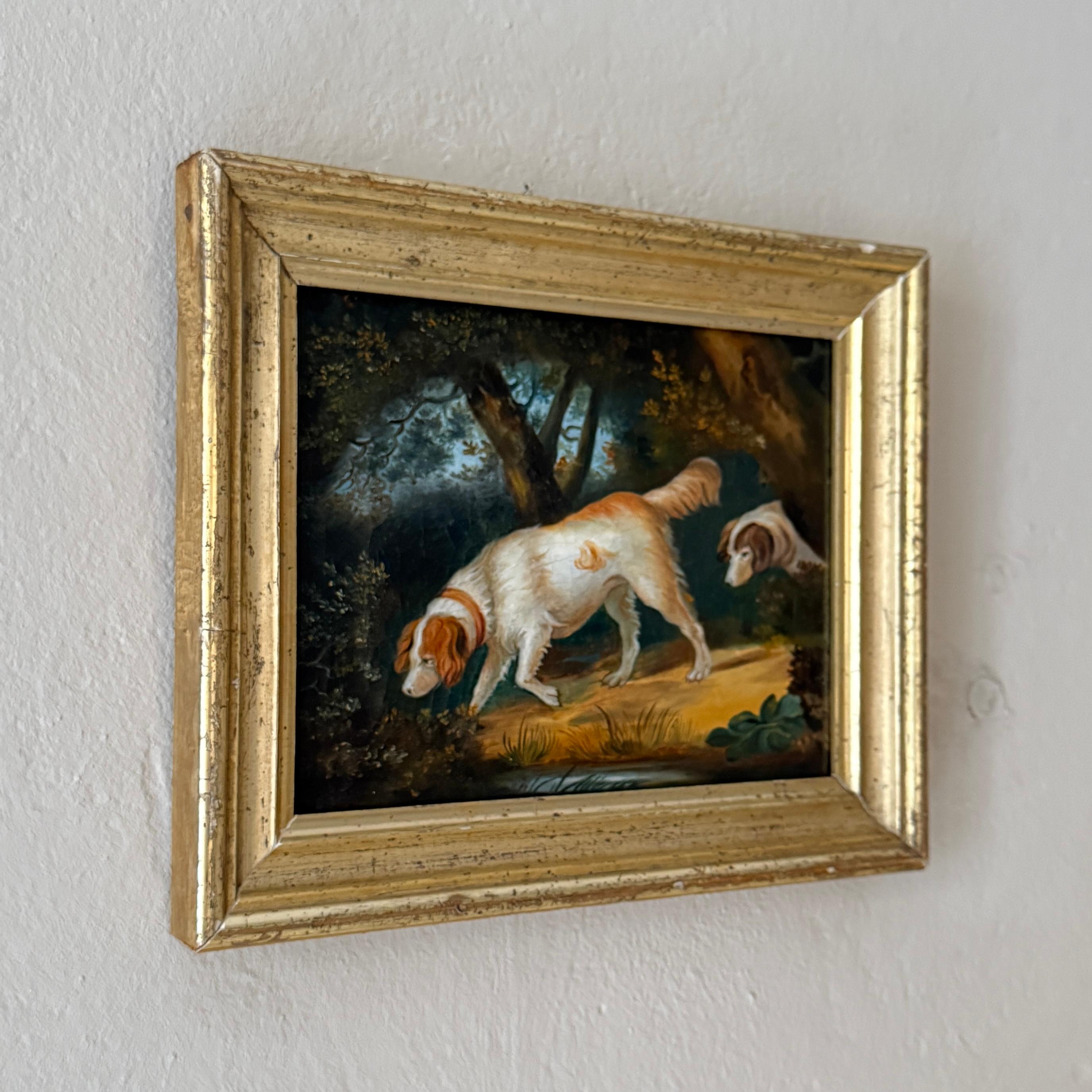 Peinture à l'huile Biedermeier des années 1820, finement exécutée, représentant une scène de chasse tranquille avec deux chiens. Peinte avec une grande minutie, la composition capture les animaux dans un cadre forestier, leurs postures alertes et