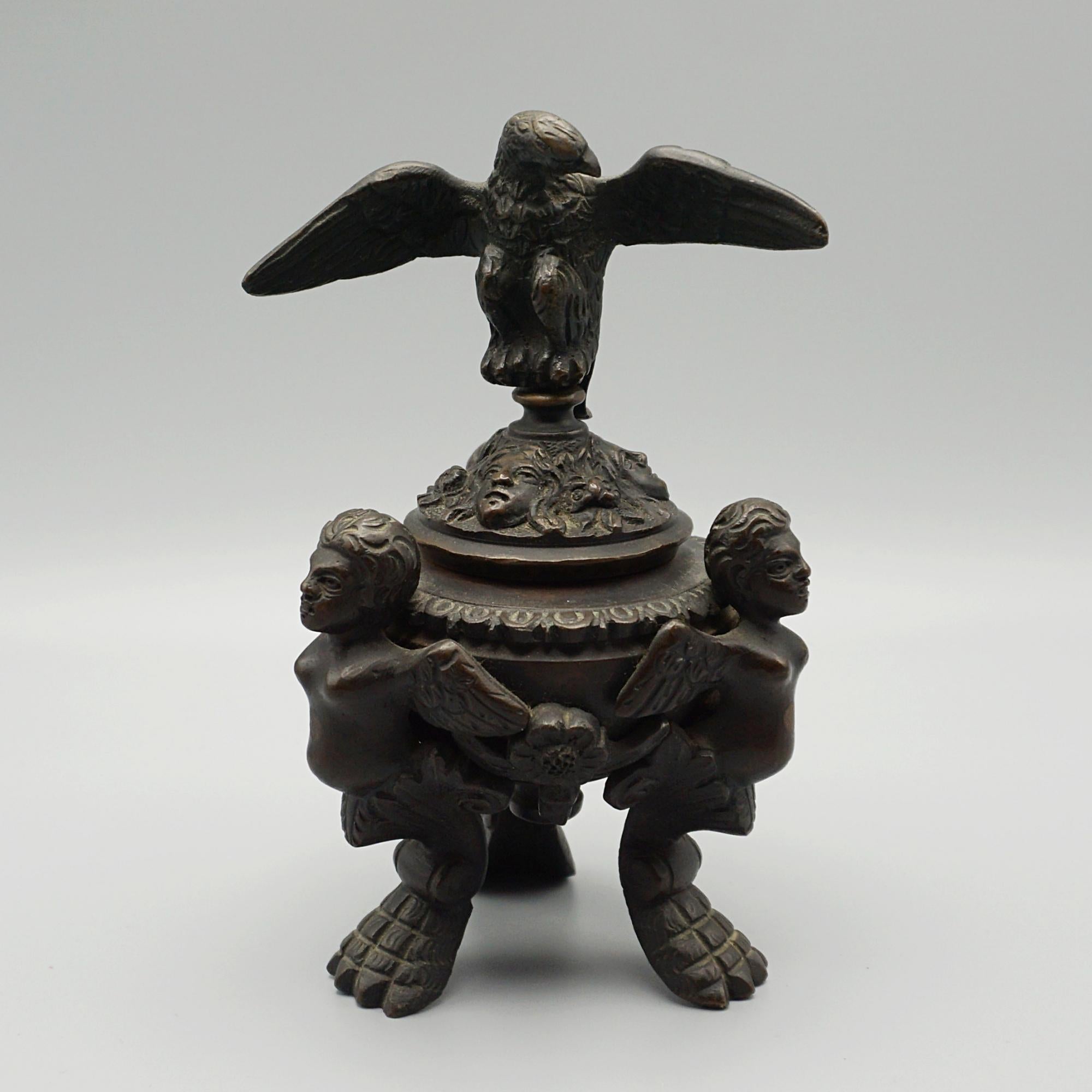 A Napoleon III bronze inkwell Encrier. Three winged cupids holding up a bowl with masked faces with an eagle standing atop. 

Dimensions: H 16cm W 11cm D 8cm 

Origin: French

Date: Circa 1820

Item Number: 2103243