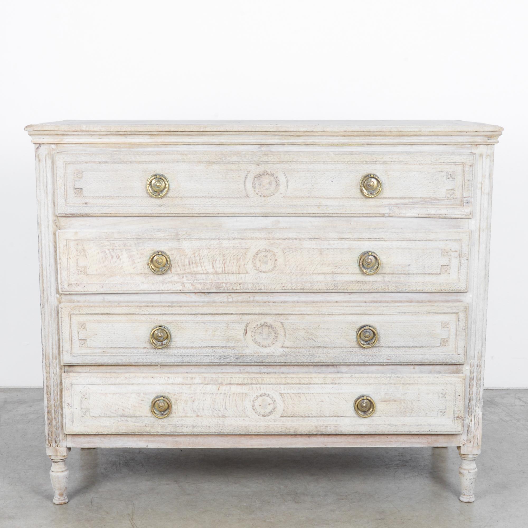 This oak chest of drawers was made in France, circa 1820. It houses four drawers, each with a carved wreath between decorative brass ring pulls. The drawers are slightly elevated, standing on angular rear legs and turned front legs. With the fine