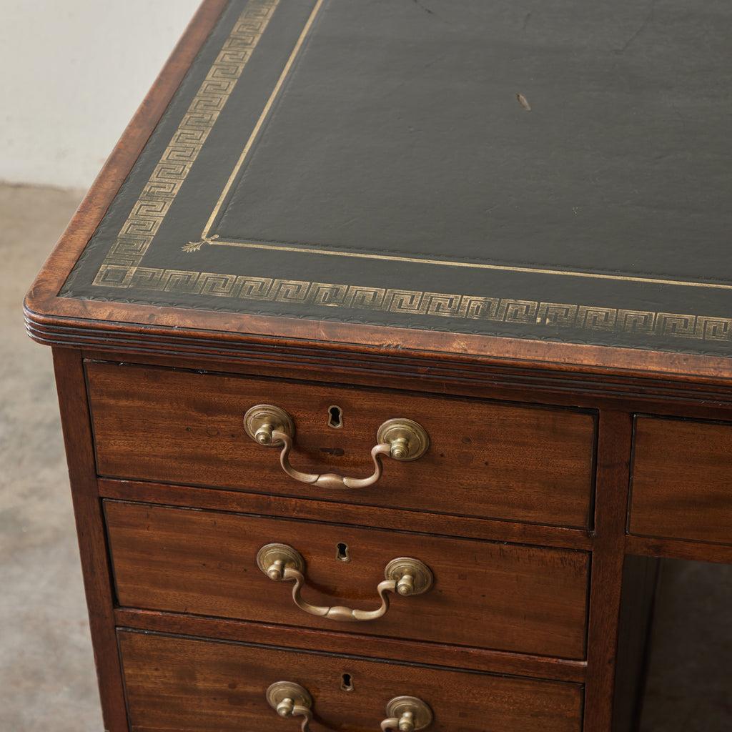 Early 19th-century English mahogany partner's desk. A tooled gilt Greek key pattern borders the molded black leather top, and on either side, two sets of four stacked drawers and one central are appointed with brass locks and drop-handle pulls.