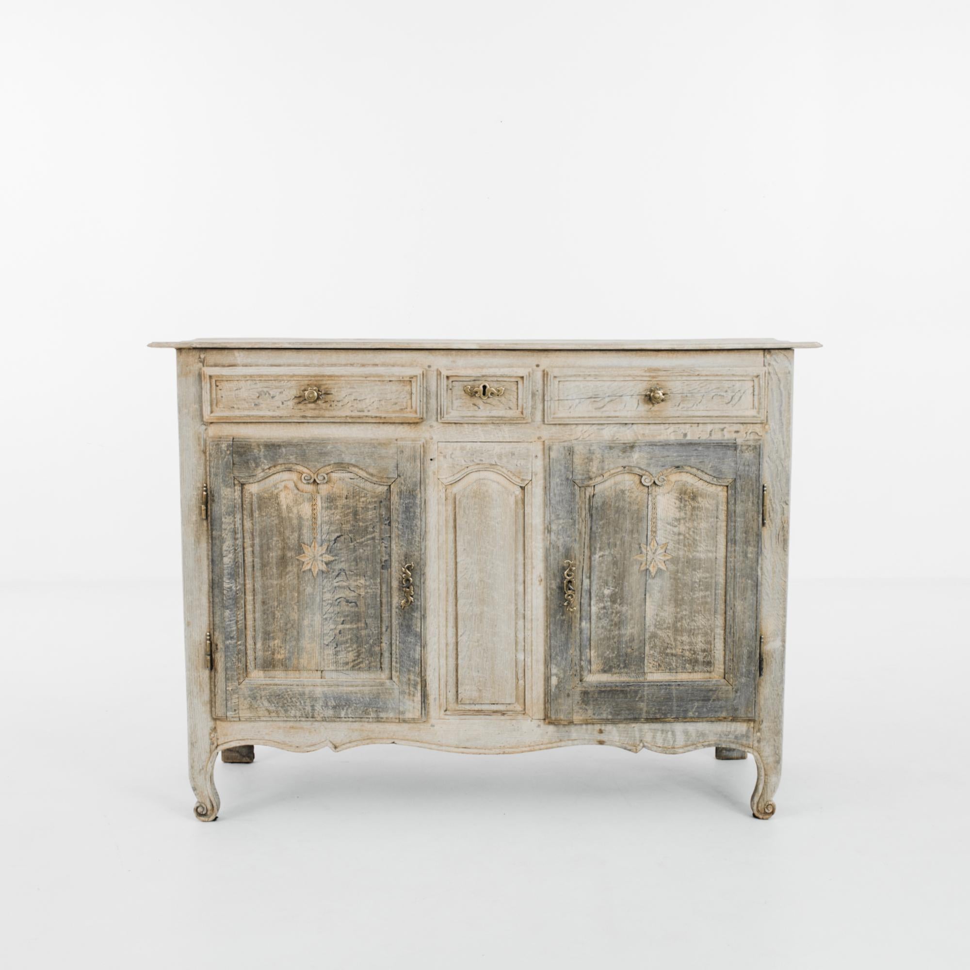 This bleached oak buffet with a scalloped apron was made in France, circa 1820. It houses three drawers, and lockable doors below open to reveal two shelves. The paneling is carved with dangling eight-point stars and adorned with scrolled arcs,