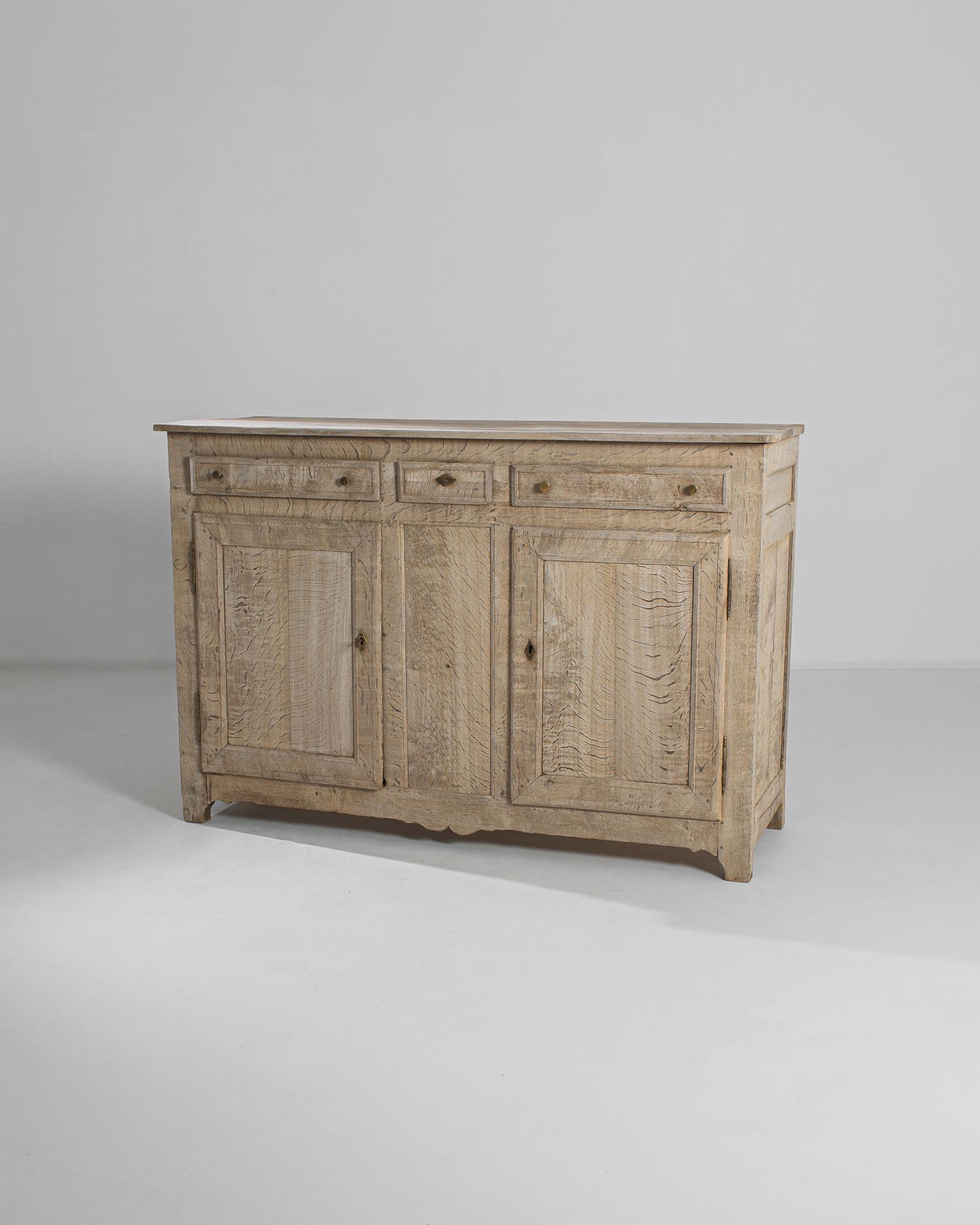 This bleached oak buffet was made in France, circa 1820. The clean design is marked by discreet ornamentation, allowing its pleasing rustic tone and exquisite wood grain to take center stage. Geometric brass pulls and lockplates, combined with the