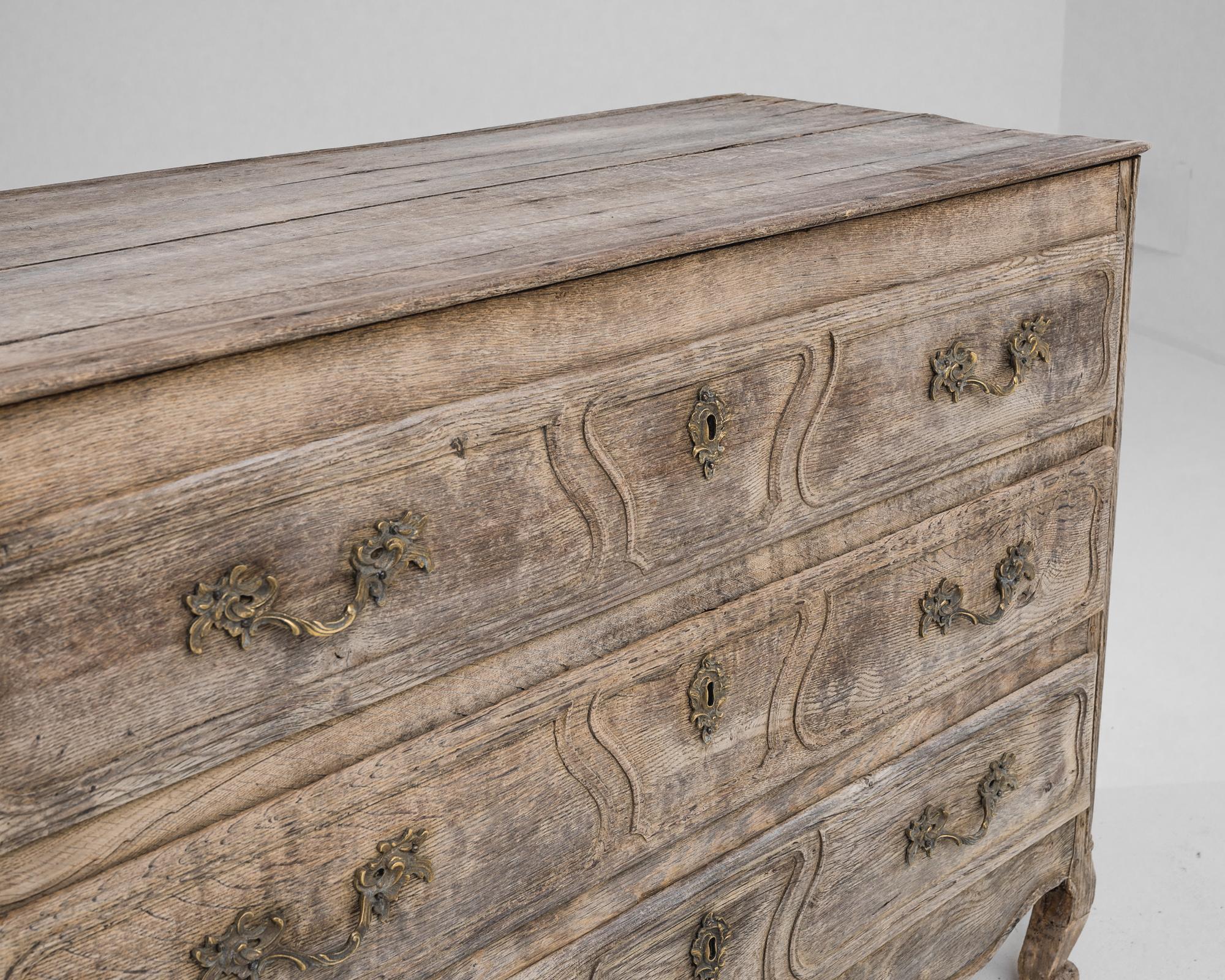 An antique chest of drawers produced in France, circa 1800. This bleached oak buffet displays three broad sliding drawers ornamented with engraved patterns, a scalloped apron and two front cabriole feet. The elaborate pulls and escutcheons made of
