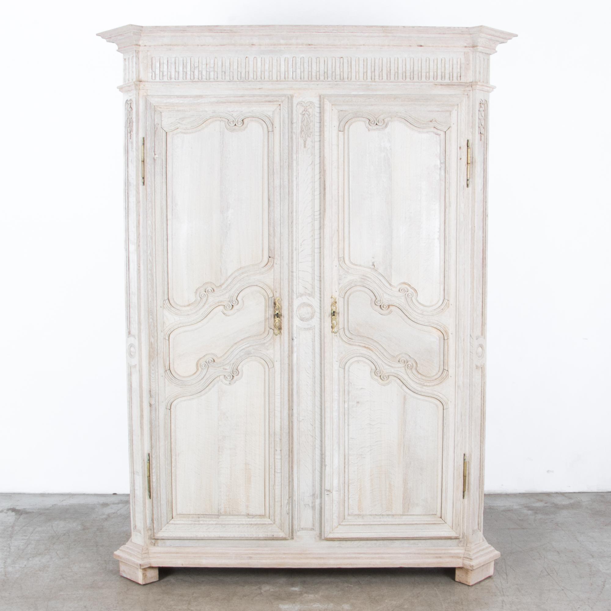 A Louis XVI influenced wardrobe from France, circa 1820. A spacious wide cabinet for wardrobe, pantry or other large storage. Time tested traditional craftsmanship in old growth European oak, with original brass hardware. A distinctive light finish