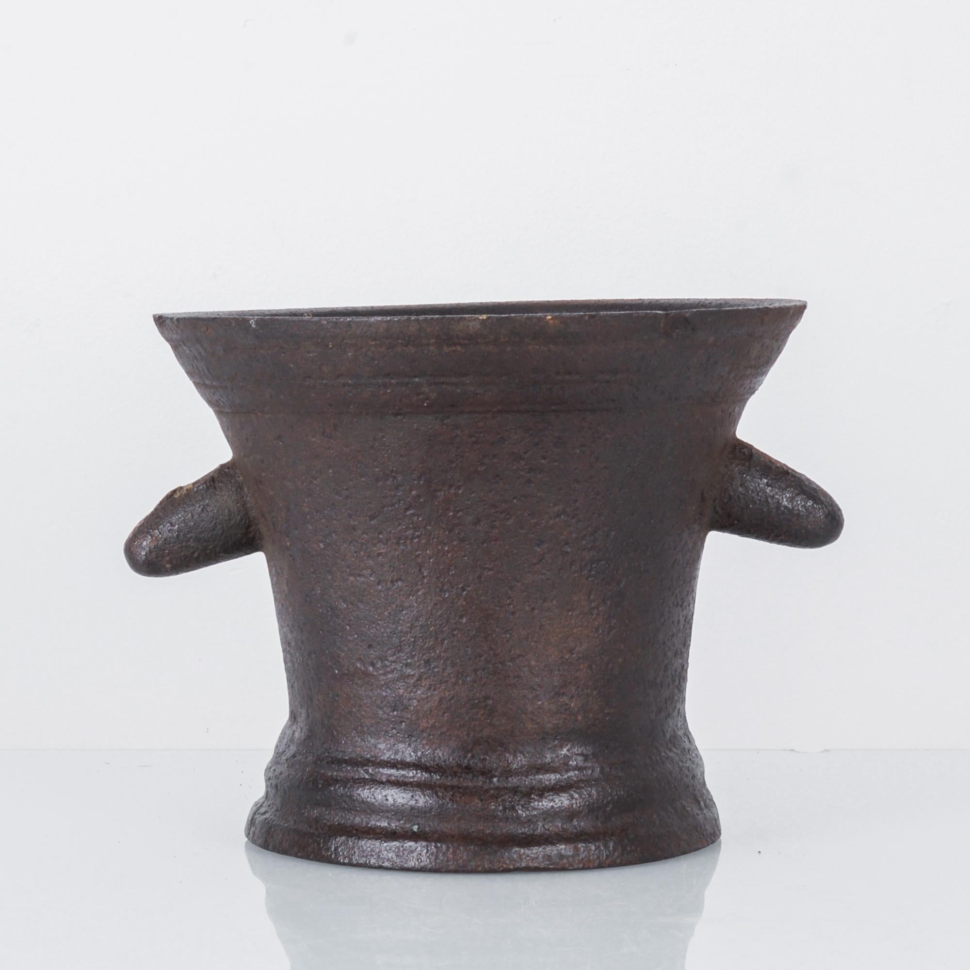 A cast iron mortar from France, circa 1820. A cup-shaped vessel with a heavy base and brim, cast in a dark metal with warm red tones and a speckled grain. Two stubby, downturned handles lend an almost anthropomorphic effect, suggestive of an