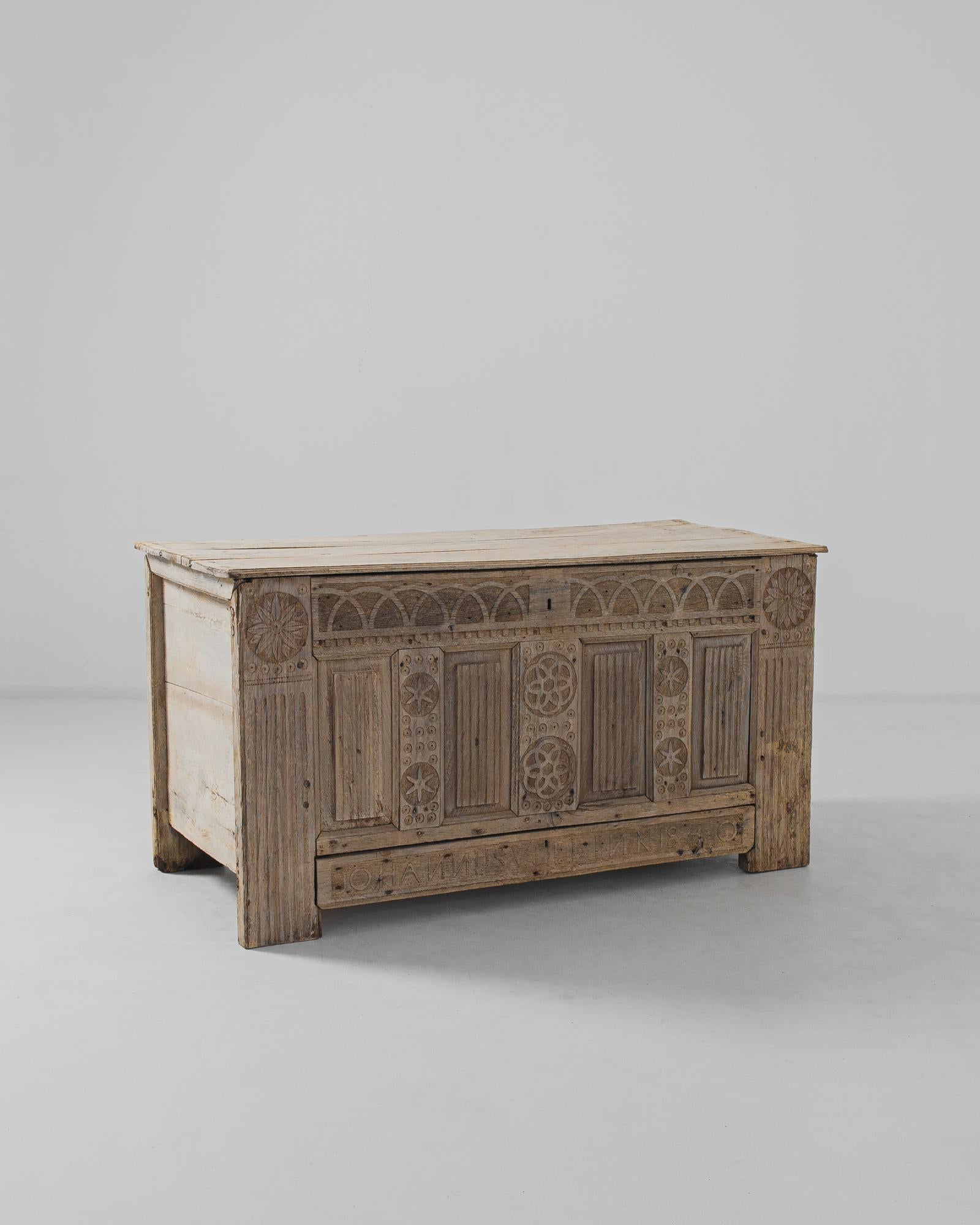A carved oak trunk from 1820s France. Carved arches, stars and rosettes echo the forms of gothic tracery, lending the sandy wood a Gothic Revival aesthetic. A long drawer below the central chest is carved with the name of the original owner and the