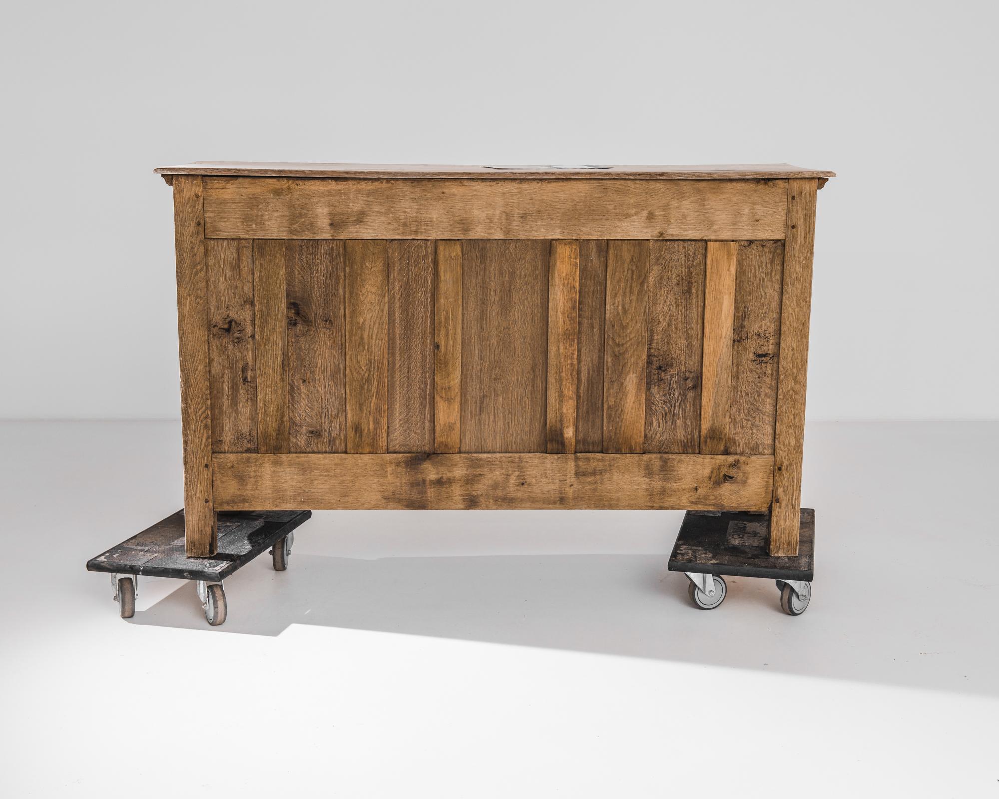 An oak buffet from 1820s France. Expressive panelling on the cupboard doors is echoed in the curves of the scalloped apron and carved central motif. The bright russet tone of the restored oak gives a fresh finish to this antique piece; gilded drawer