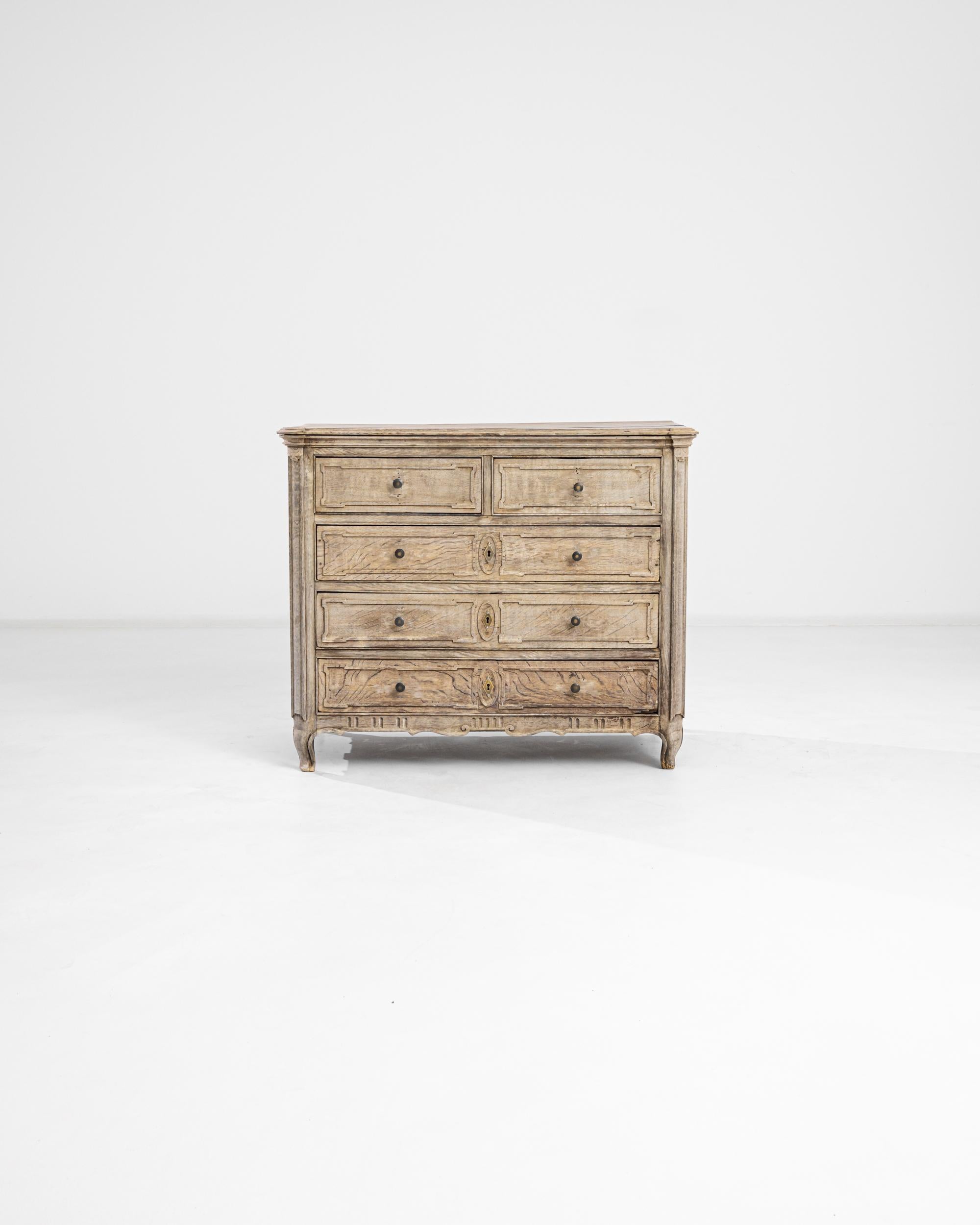Elegant paneling in natural oak gives this chest of drawers an air of serene sophistication. Built in France in the 1820s, subtle curves lend a sensuous note to the upright case — carved oval accents circle the diamond-shaped lock pieces; cabriole