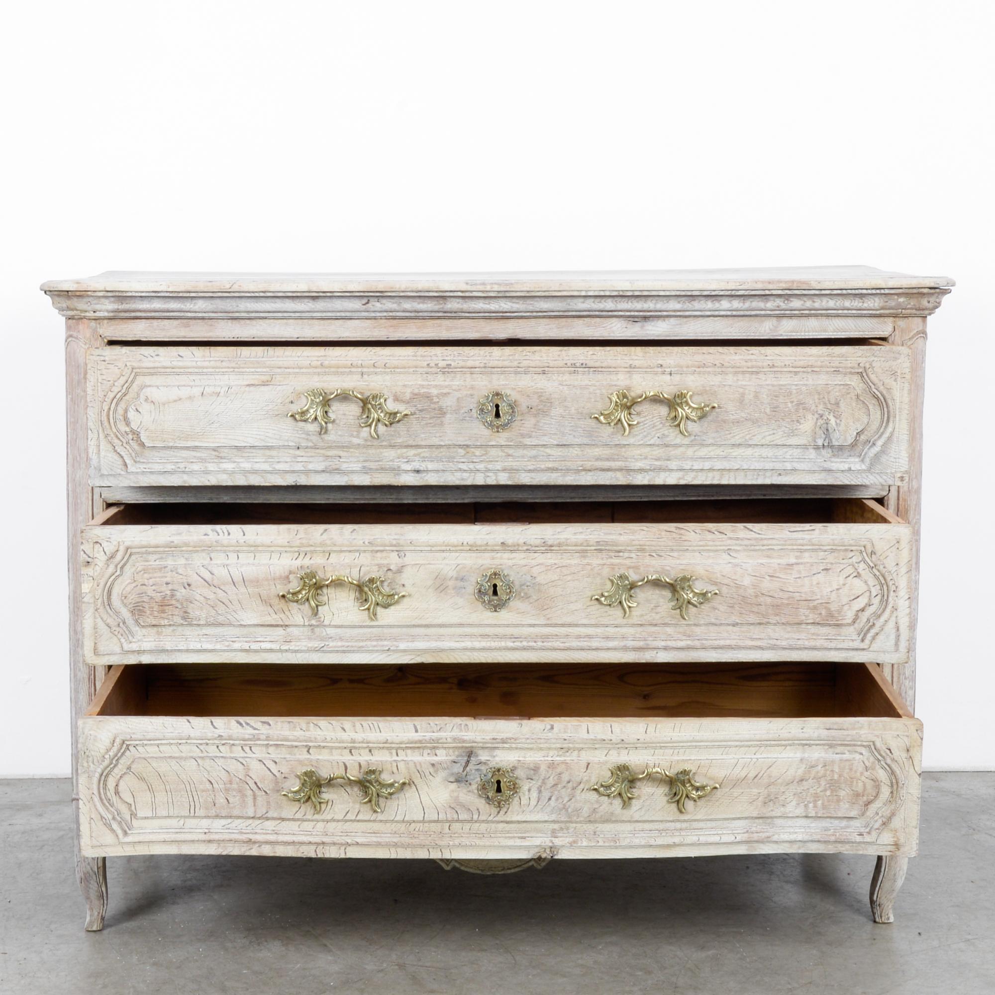 This bleached oak chest of drawers was made in France, circa 1820. It flaunts a smooth finish, which highlights the distinctive wood grain. Elevated on cabriole legs, the chest features three drawers with decorative locks and pulls. The scalloped