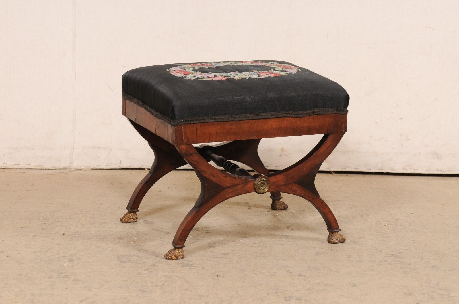 An Italian carved wood dante stool with upholstered seat from the early 19th century. This small bench from Italy, circa 1820's, has been designed in the typical dante style with legs consisting of two half-moon shapes, which attach at their rounded