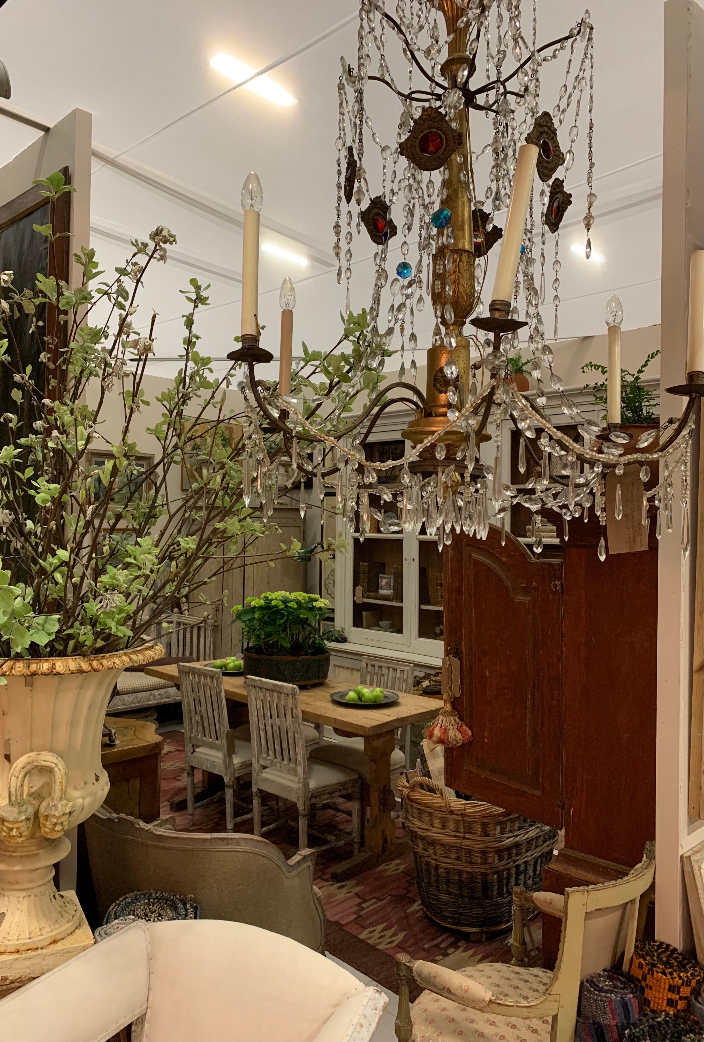 A handsome and decorative Italian six branch circa 1820 chandelier from Genoa region. 
Its central turned wood column support is segmented, gilded and has stylised anthemion decorative detail that is swathed  with swags of clear glass beads and
