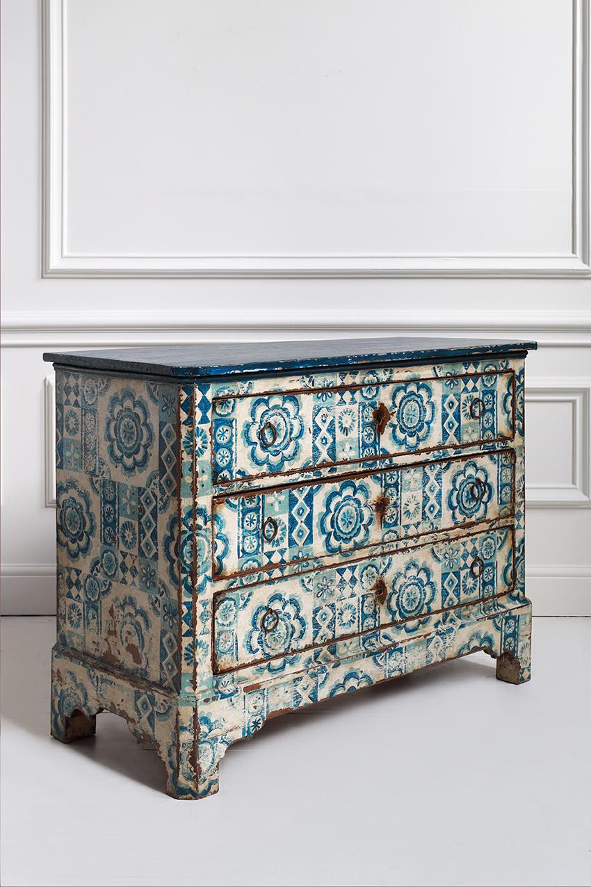 An example of early 19th-century decorative work, this commode marries continental Neoclassical form with a vibrant, artisanal painted finish. The entire surface—from the fluted sides to the drawer fronts—is coated in a rich blue and white palette,