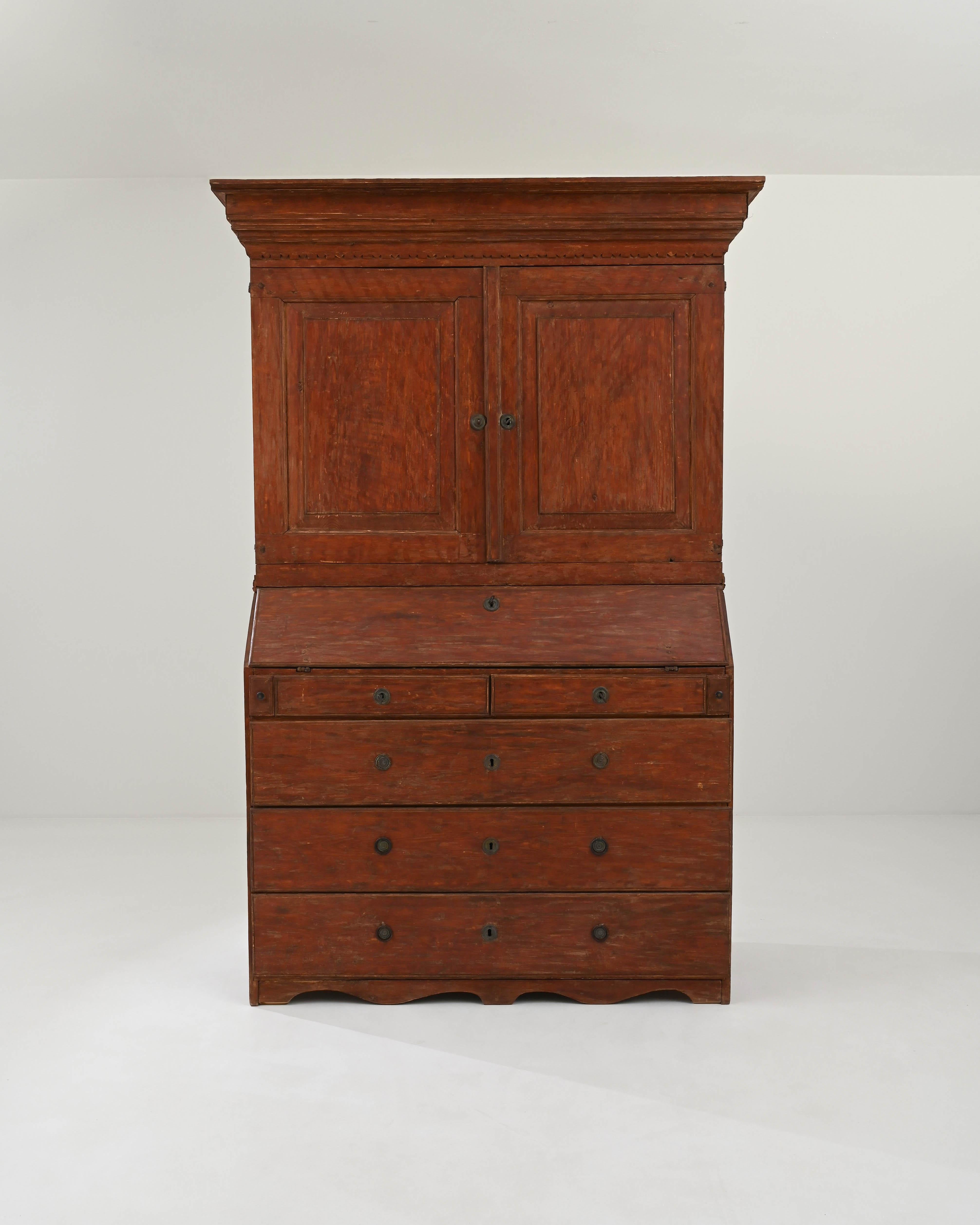 A wooden cabinet created in 1820s Sweden. Tall, slender, and painted in an inviting reddish ochre, this cabinet presents an air of familiarity and amicable function. This discreet secretary cabinet unfolds to reveal a narrow writing surface for