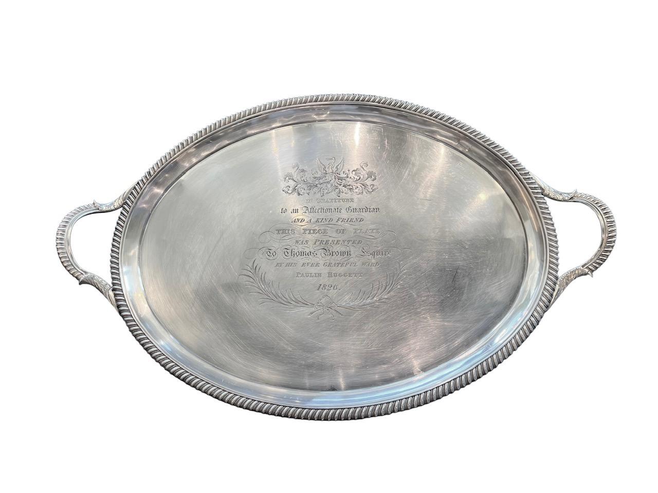 Crafted in the year 1823 in London, this remarkable English George IV silver presentation tray, expertly created by the skilled silversmith John Mewburn, stands as a testament to the artistry and elegance of its era.

Exquisitely designed, the tray