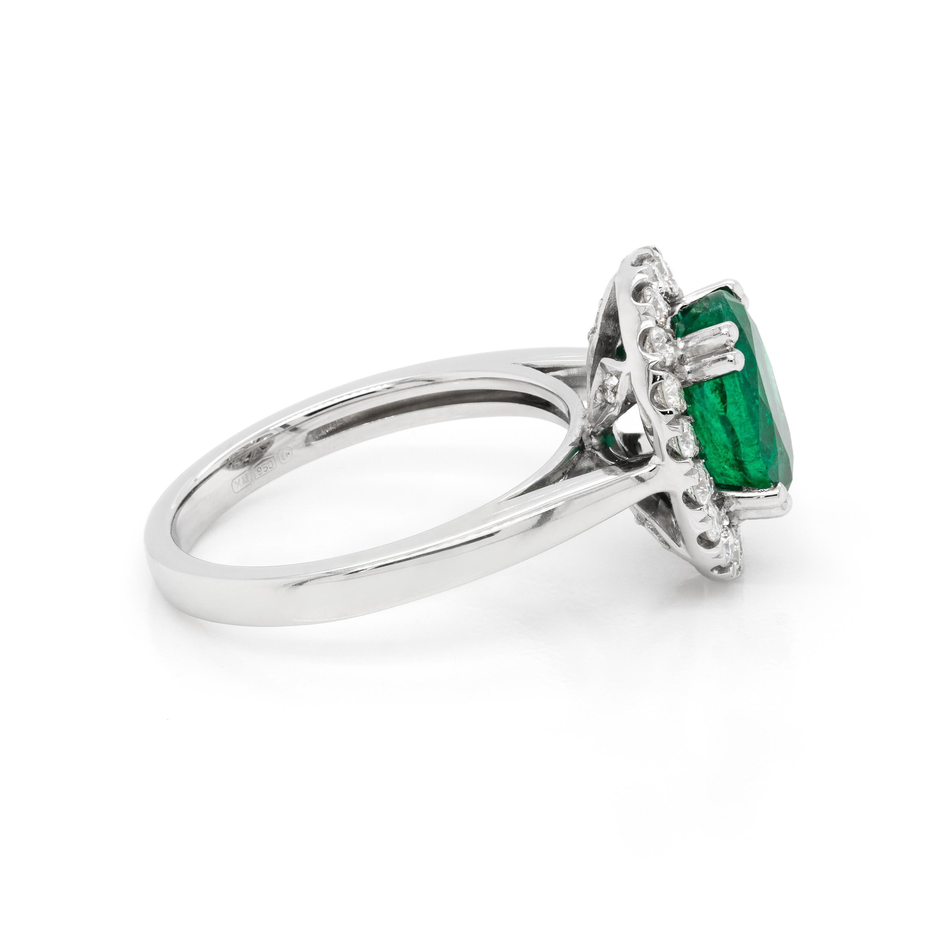 Lovely cluster engagement ring featuring a 1.83ct oval shaped emerald, in an open back, four double claw setting. The beautiful emerald is surrounded by a halo inlaid with eighteen claw set fine round brilliant cut diamonds with a total weight of