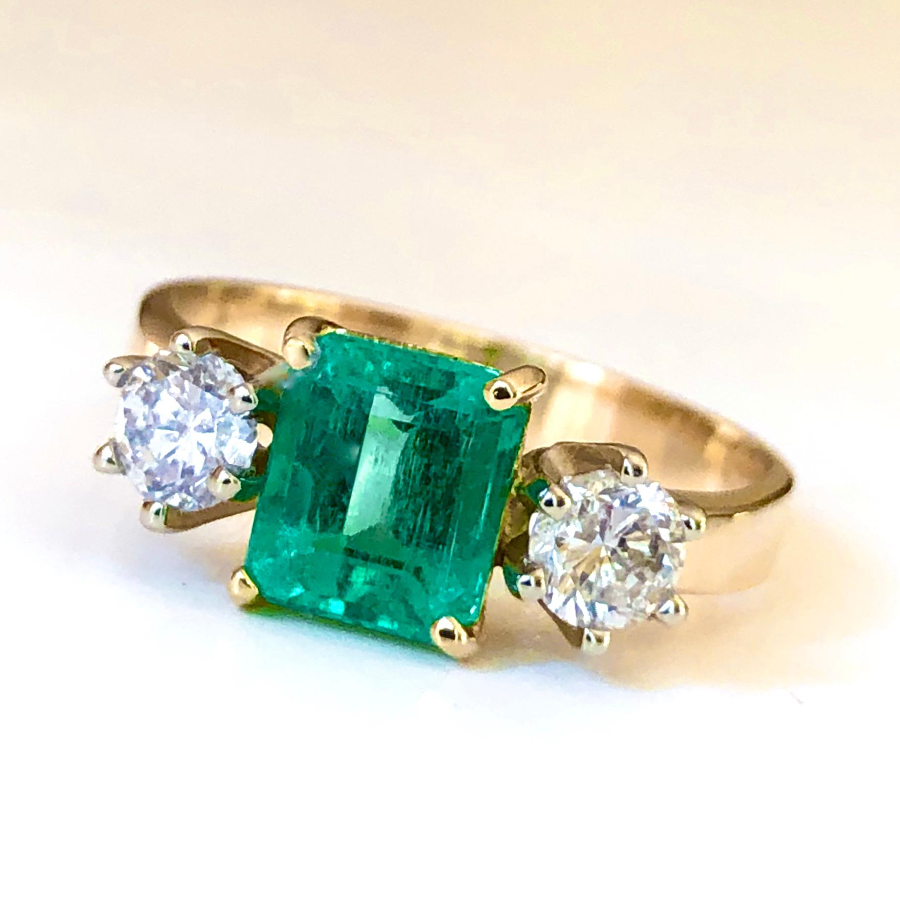 This elegant ring features a vivid AAA Colombian emerald 1.27 carat emerald cut, medium green color. Set in a 18K gold handmade, three-stone engagement ring with round brilliant cut diamonds side stones 0.56 ctw of H color and SI1 clarity, this ring
