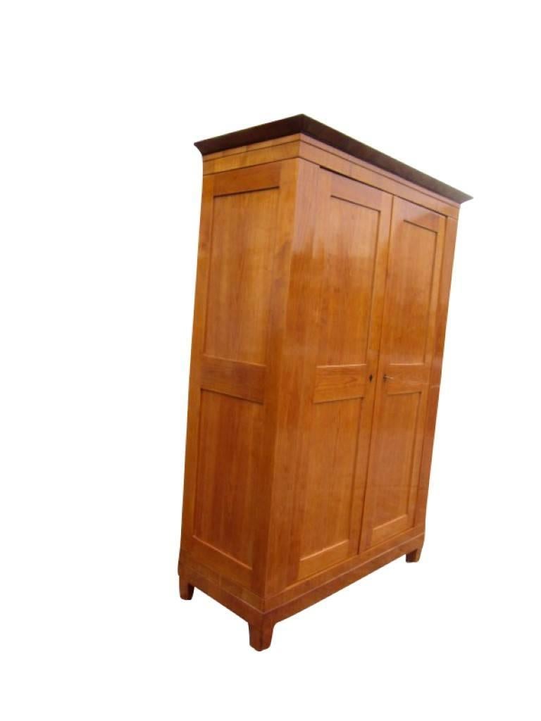 A wardrobe from the Biedermeier era with multiple types of wood. The piece convinces with a simple but elegant design and a wonderful brown wood color. The body is made of solid oak veneered with cherrywood, polished with shellac. The back wall is