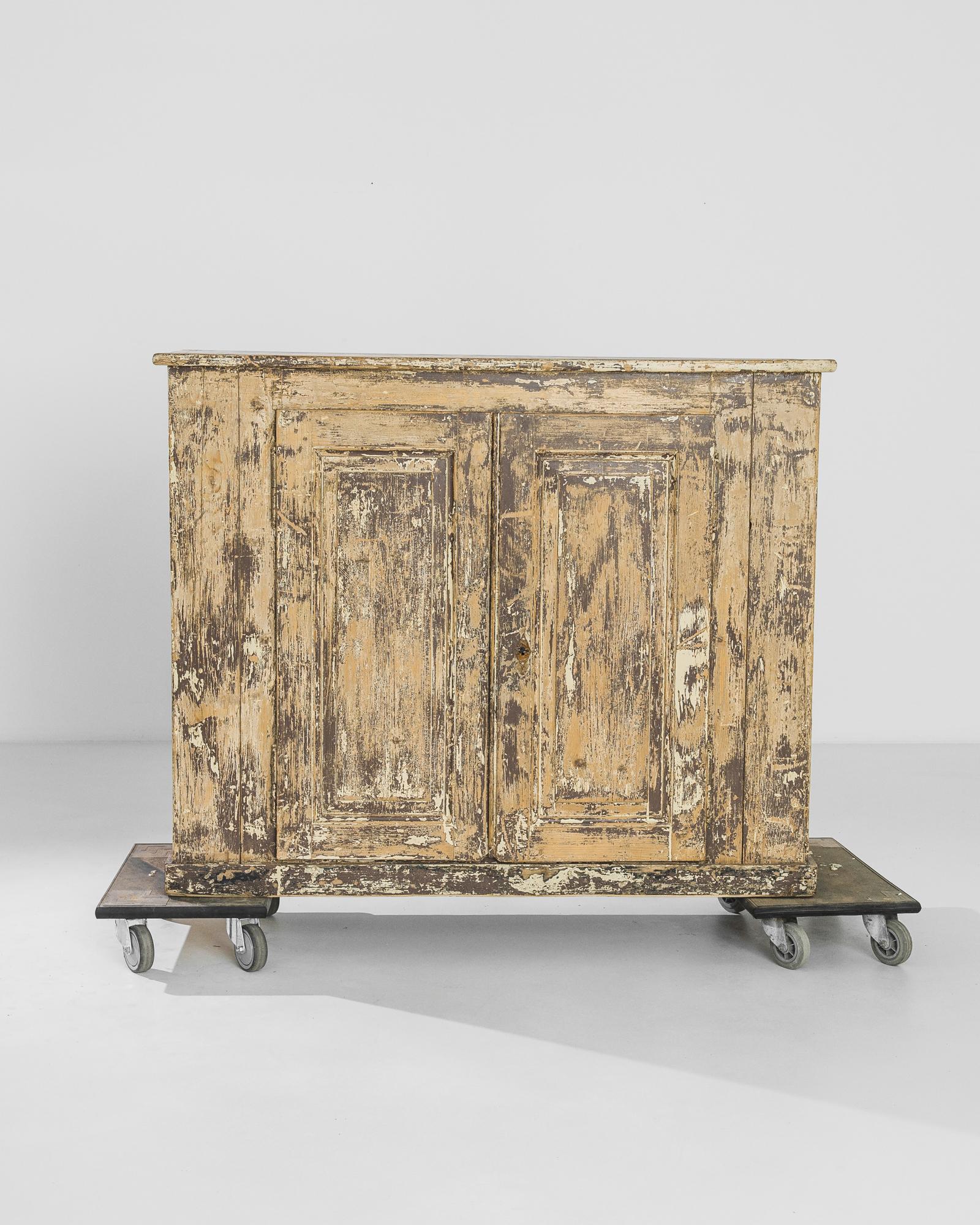 A wooden cabinet from 1830s France with an expressive patina. The surface of the wood is grazed and scraped, creating a dynamic texture and allowing glimpses of the various layers of paint and varnish that the piece has possessed over the years.