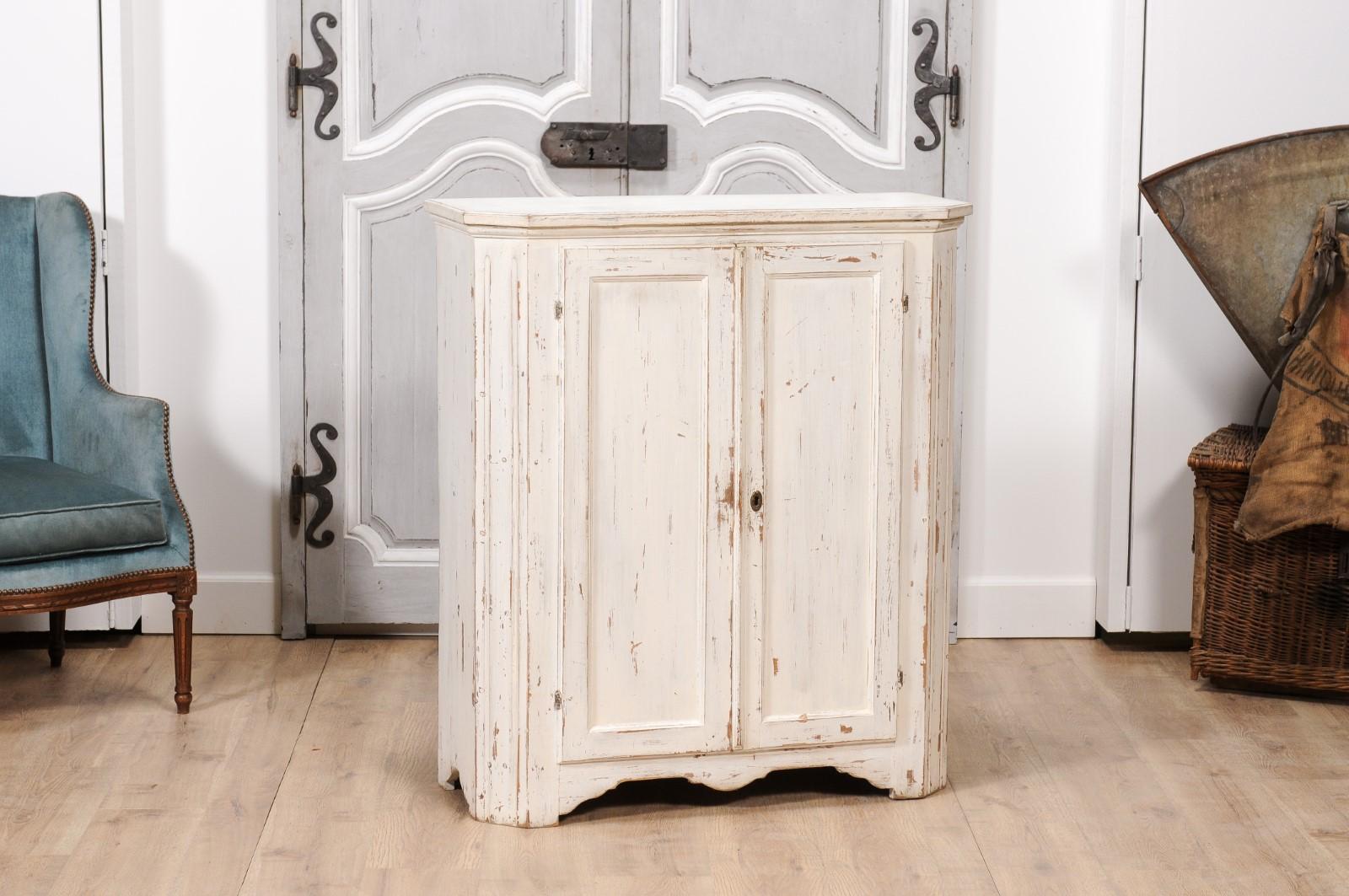 A Swedish off-white painted sideboard from circa 1830 with carved apron and distressed finish. This charming Swedish sideboard from circa 1830 is a study in grace and simplicity, with its inviting off-white painted finish highlighting a thoughtful