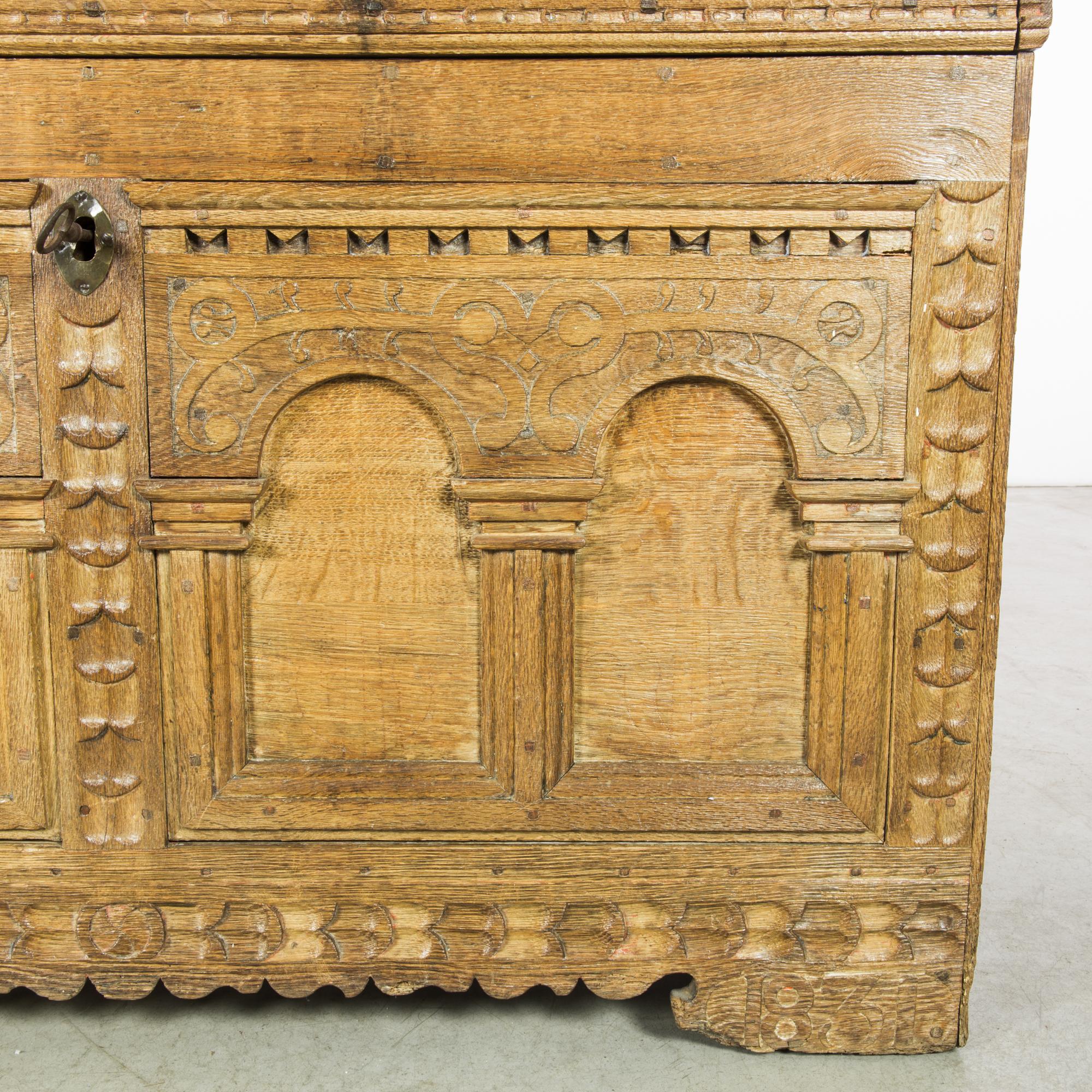 Behold the exquisite craftsmanship of this 1831 Belgian wooden trunk, adorned with its original patina that whispers the tales of time. The frieze, graced with classical arches, unveils intricate hand-carving, a testament to the artisan's dedication