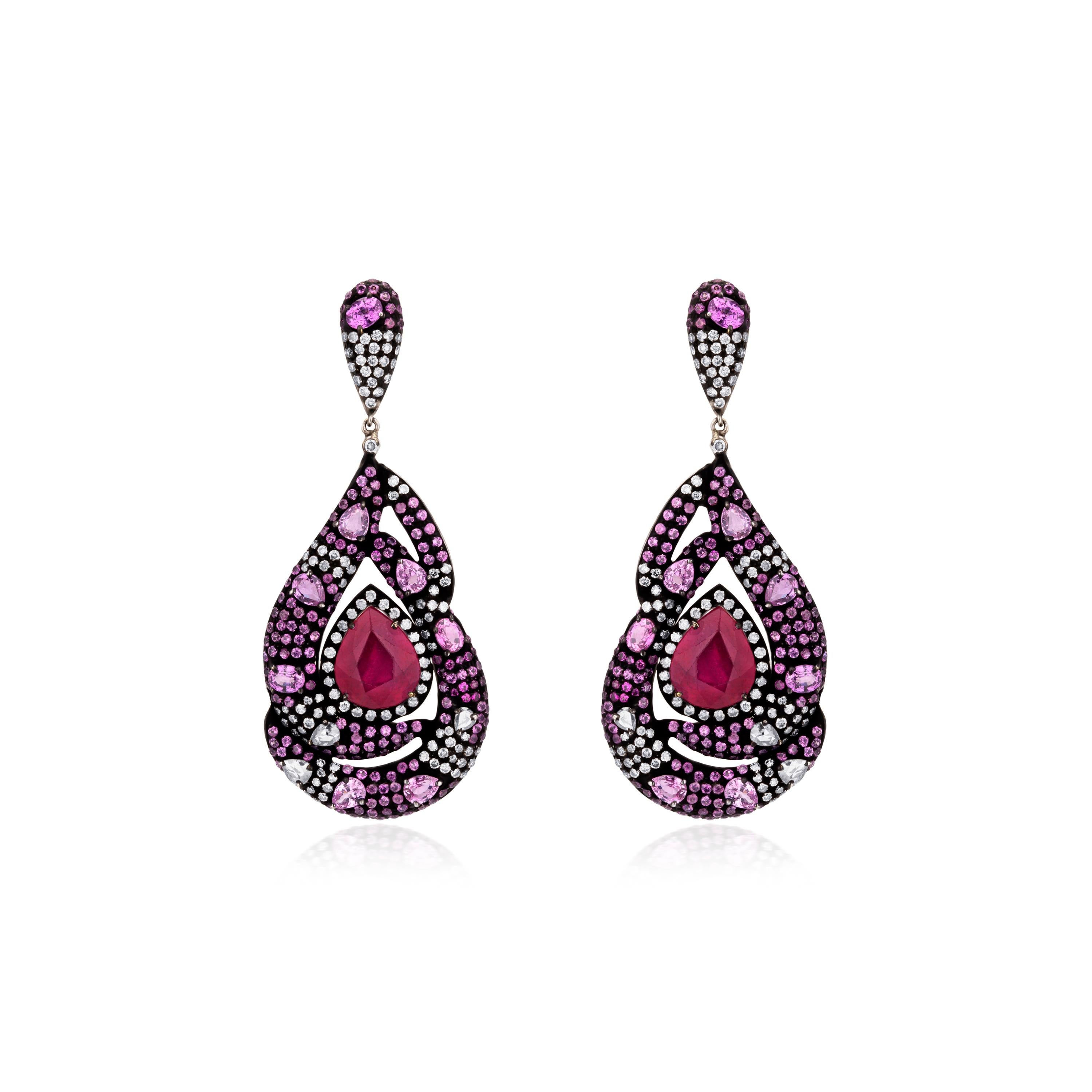  Each earring is composed of one pear cut ruby framed within elongated curvilinear drops embellished with pink sapphires and diamonds. The drops present a picture of a mythical snake protecting a precious stone. The black rhodium finish bestows