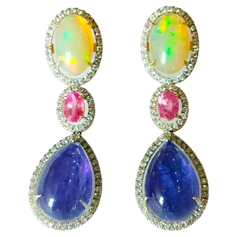 Boucles d'oreilles pendantes en or 18 carats et diamants, composées d'opale, de saphir rose et de tanzanite. Le poids du cabochon de tanzanite est de 18.35 carats. Les tanzanites proviennent de Tanzanie de manière responsable. Le poids de l'opale
