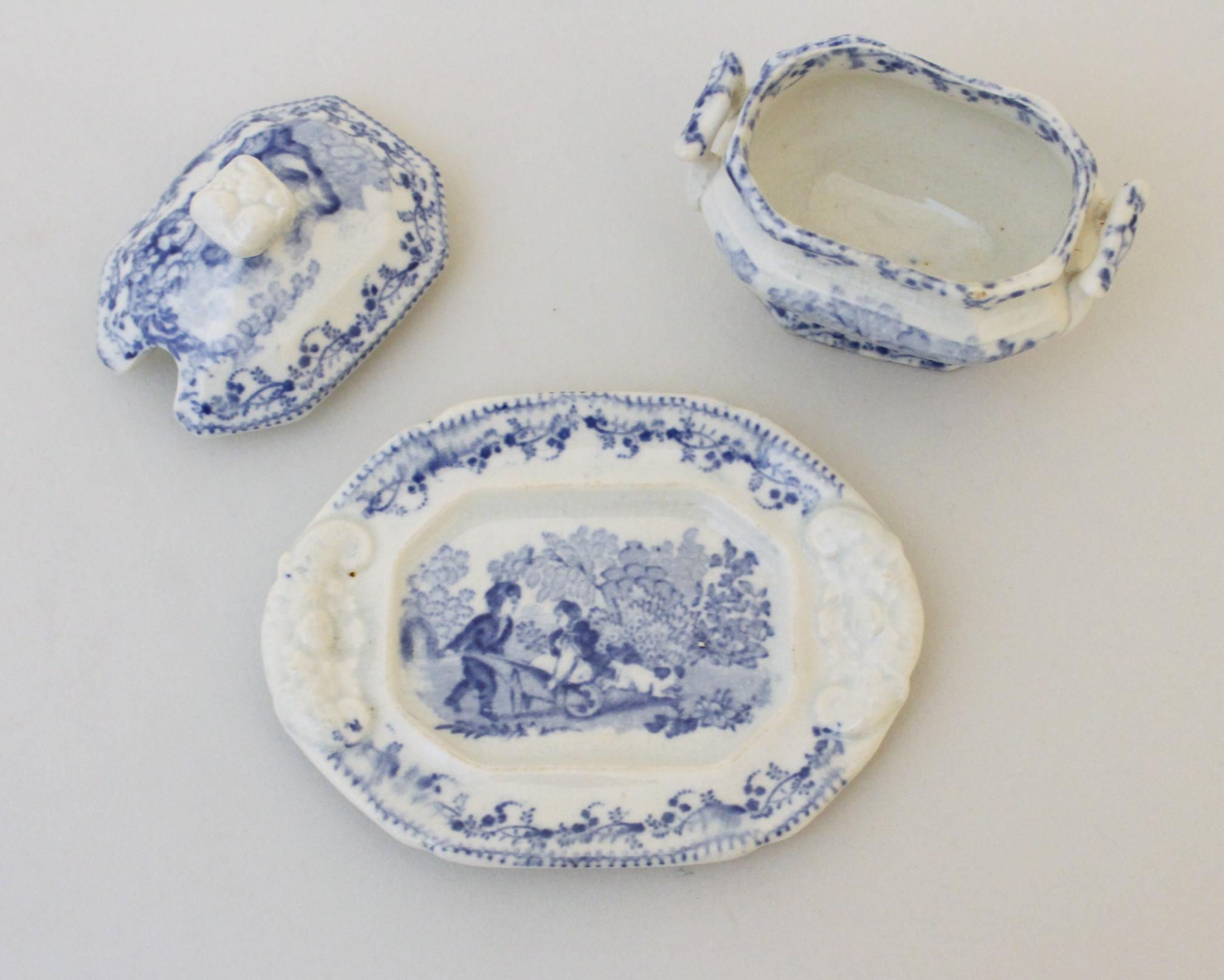 Es handelt sich um eine Sammlung von 5 Kindergeschirrteilen, um 1840. Die Stücke sind in Blau und Weiß gehalten und zeigen das charmante Motiv eines Jungen, der seine Schwester im Rollstuhl mitnimmt. Das Set besteht aus einer Suppenterrine, einer