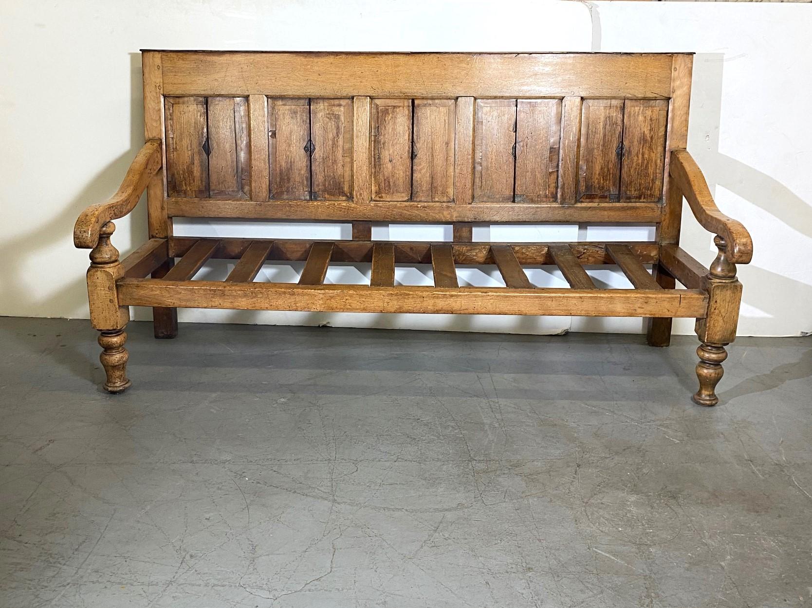An English 1840 bench. Raised chamfered panels to the back. Dowl peg construction. Turned legs and arm support with loose cushion. New upholstery.