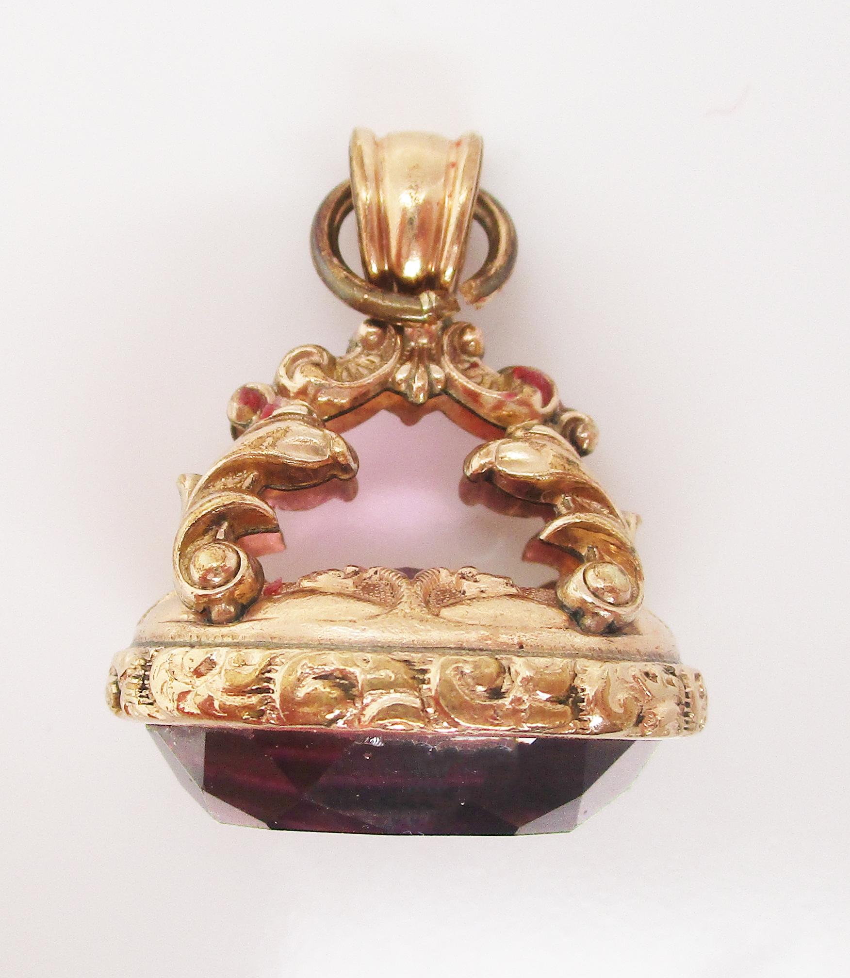 This stunning Georgian pendant is from 1840 and features bright gold and a great amethyst! The fine details of the charm curl upward from the base in the form of an arching cathedral element, subtle milgraining, and textured engraving. The detail in