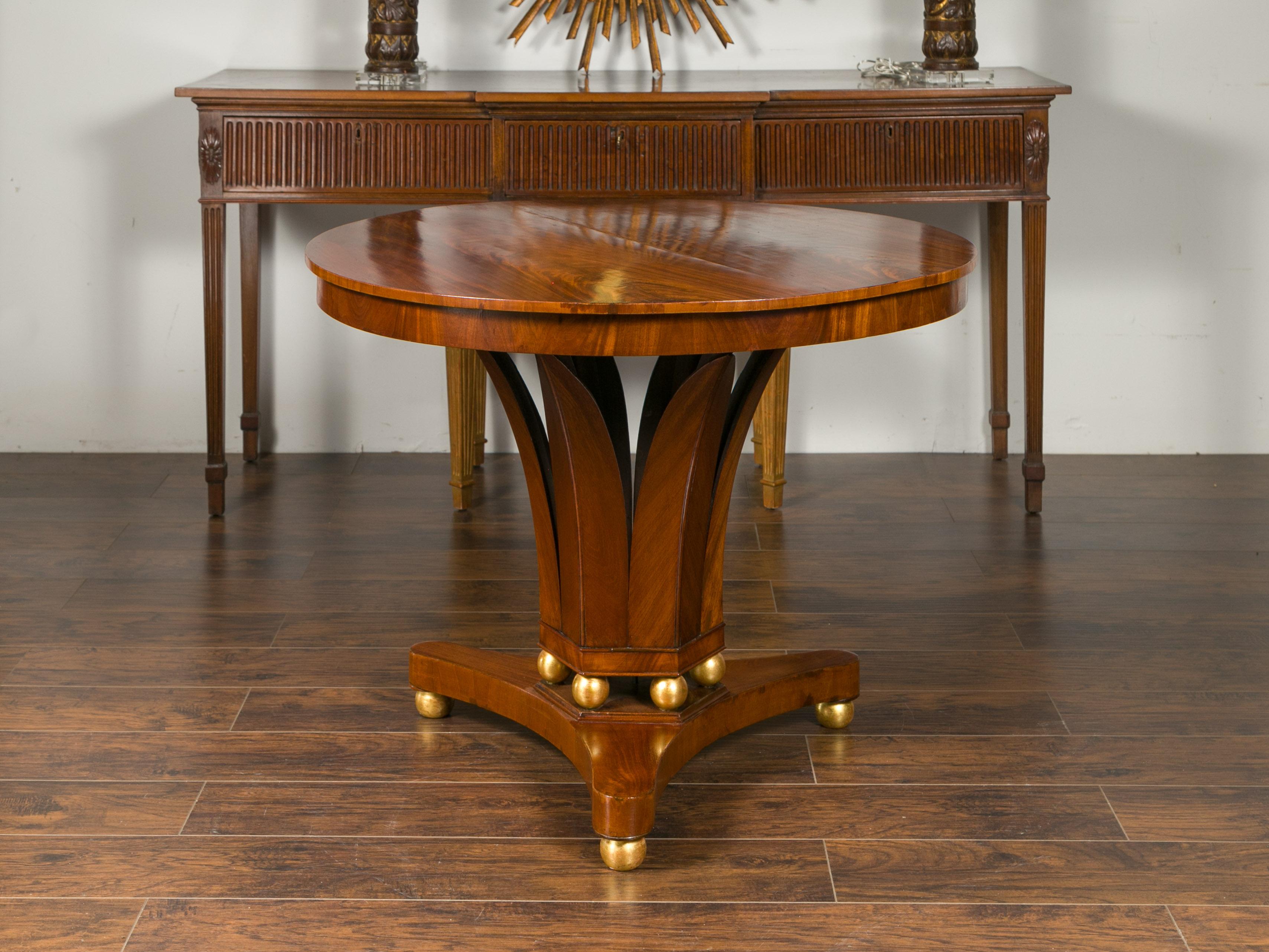 An Austrian Biedermeier period walnut center table from the mid-19th century, with giltwood spheres and foliage style base. Born in Imperial Austria during the second quarter of the 19th century, this exquisite walnut table features a circular