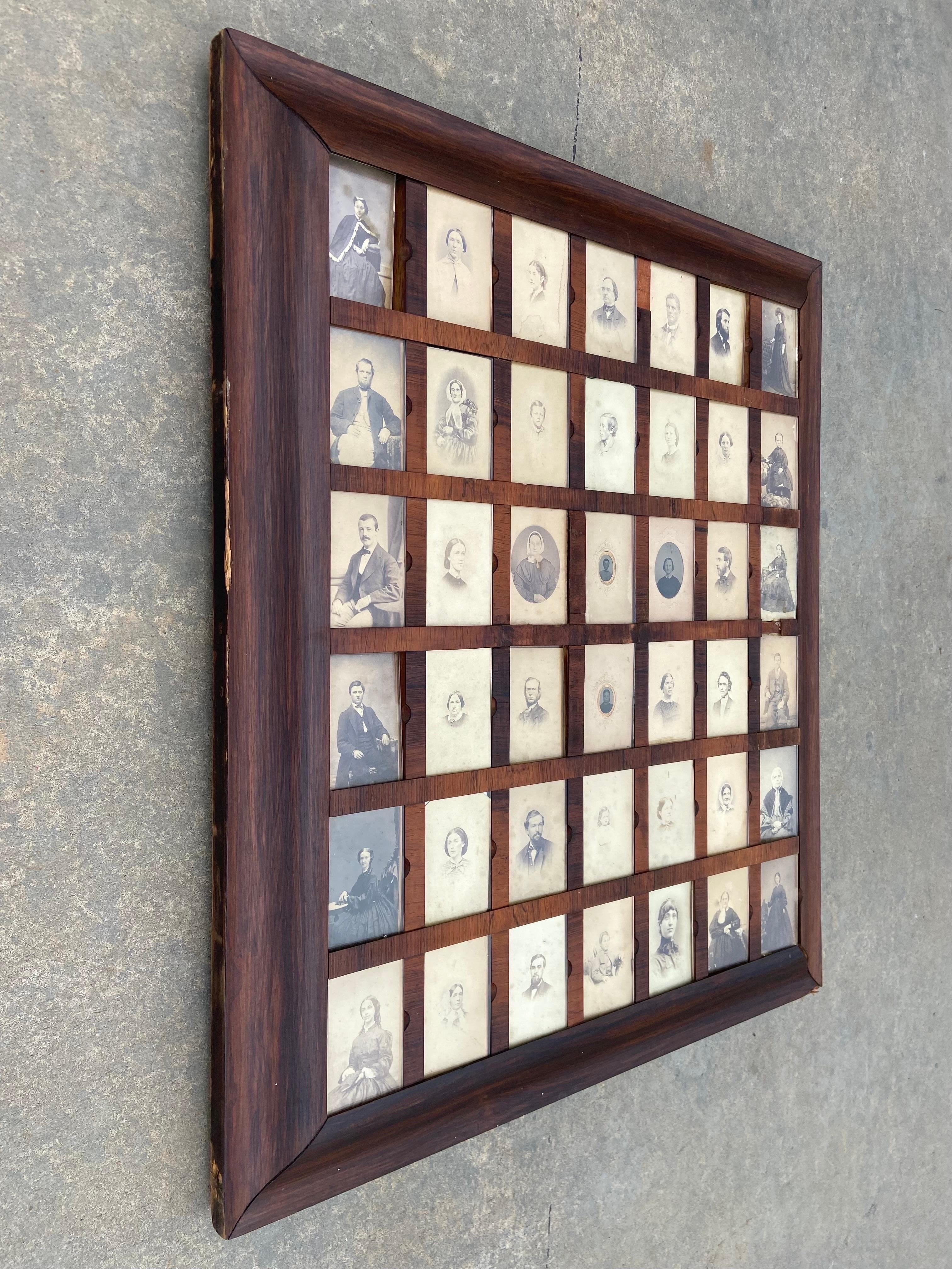 An antique, American Empire era hand made picture frame cabinet containing a collection of forty two black and white photographic images, which could very well be all images of an extended family. Each photograph measures approximately 2.25