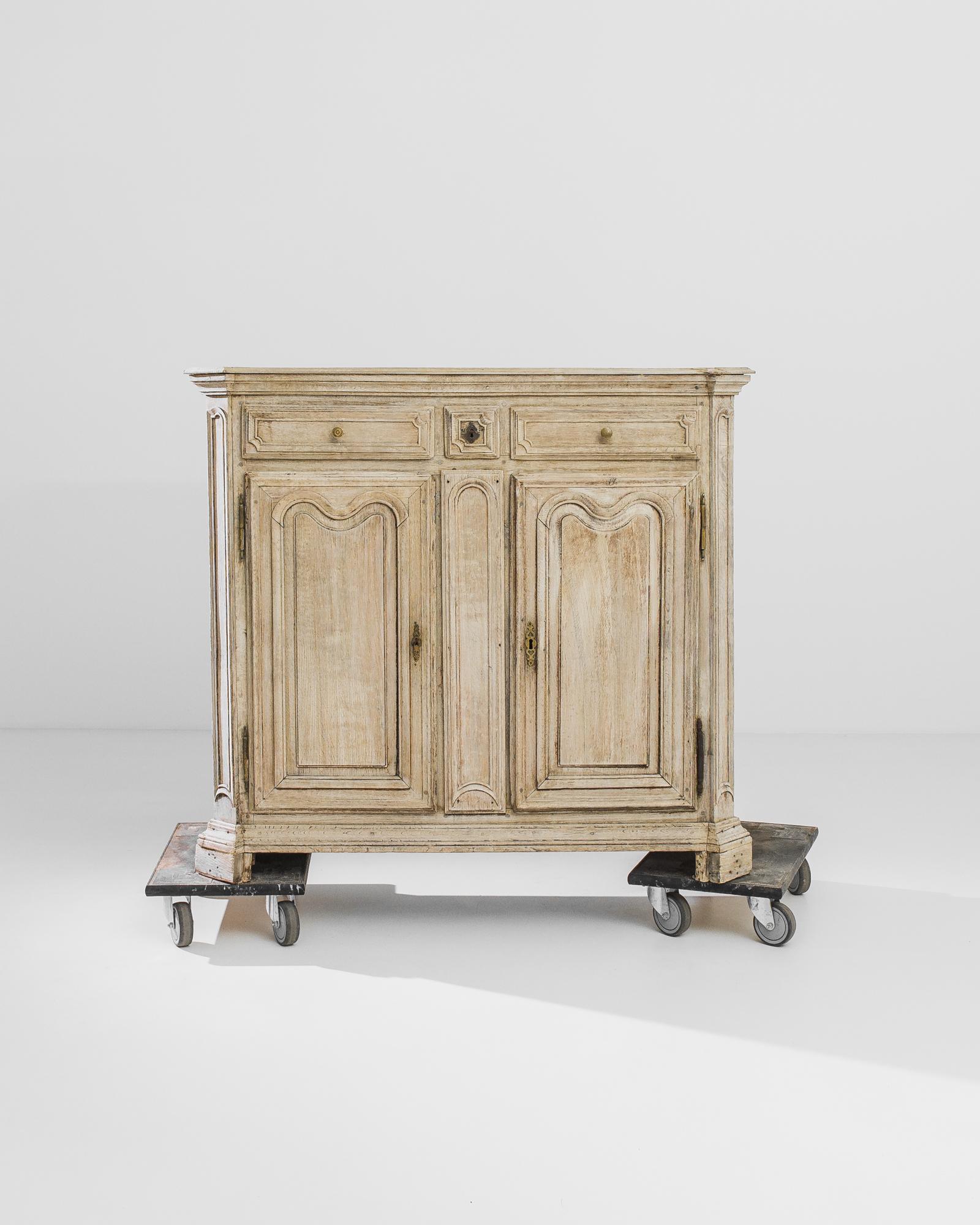 A bleached oak buffet from France, produced circa 1840. With a Neoclassical elegance, this buffet rises from the ground like a column on Mt. Olympus. The lyre inspired panels fronting the doors to the two shelf cabinets flanking the joyous,