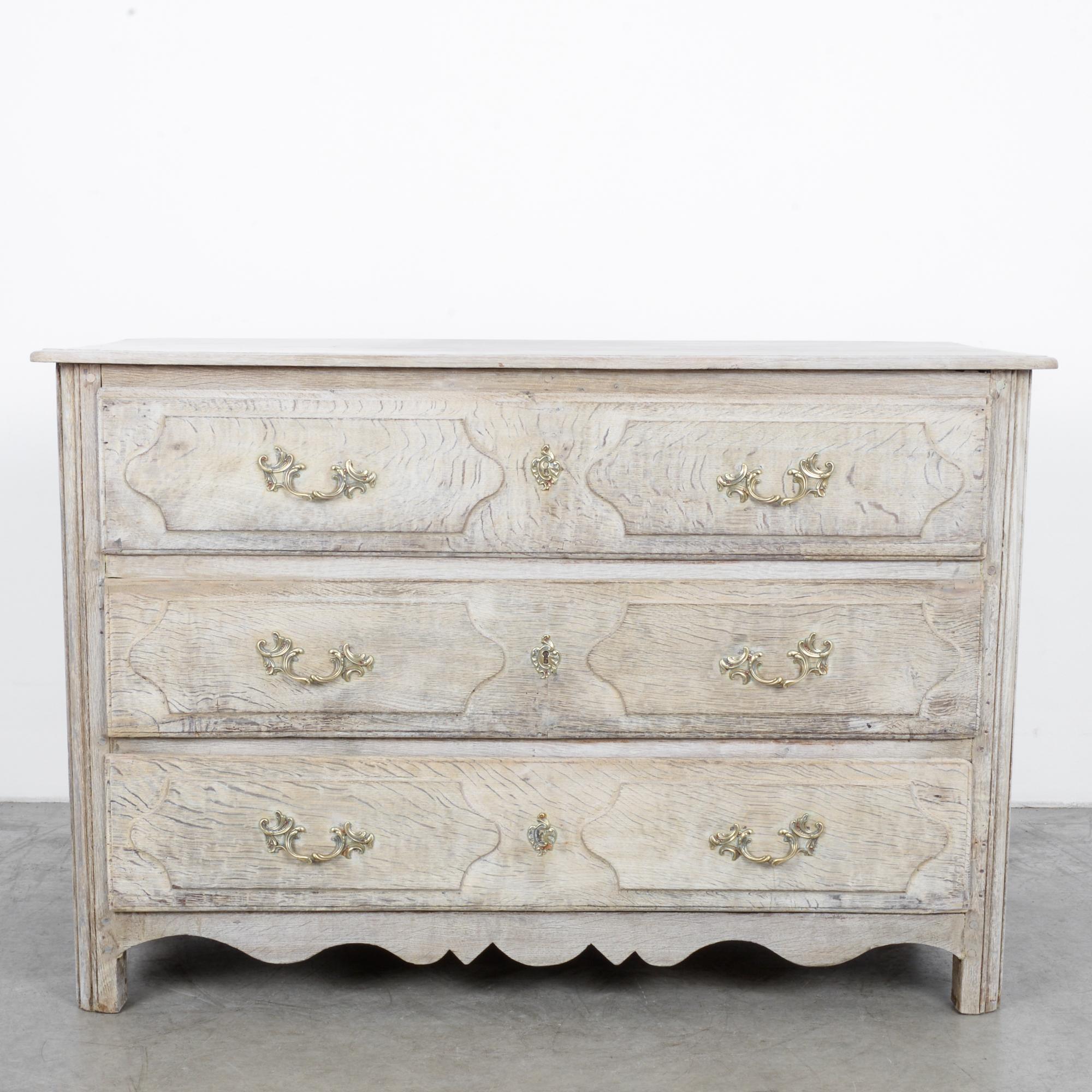 A French oak chest of drawers, circa 1840. These three oak drawers with gilt bronze escutcheons are undergirded by a scrolled apron. The rustic design is complemented by the sylvan swirls of the knobs over raised panel drawer fronts.