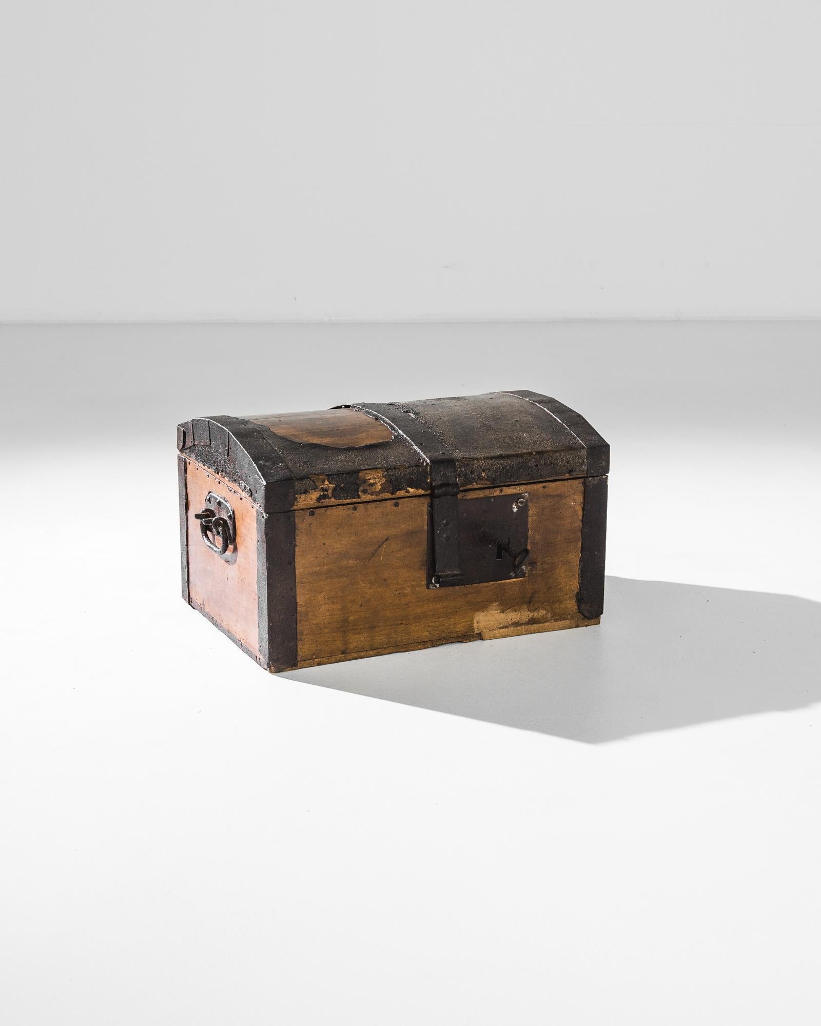 A wooden trunk from 1840s France. The arched lid, reinforced with iron bands, creates a treasure chest silhouette; the timeworn finish of the metal overlay accentuates the sense of mystery and romance. Drop handles on either side allow for ease of
