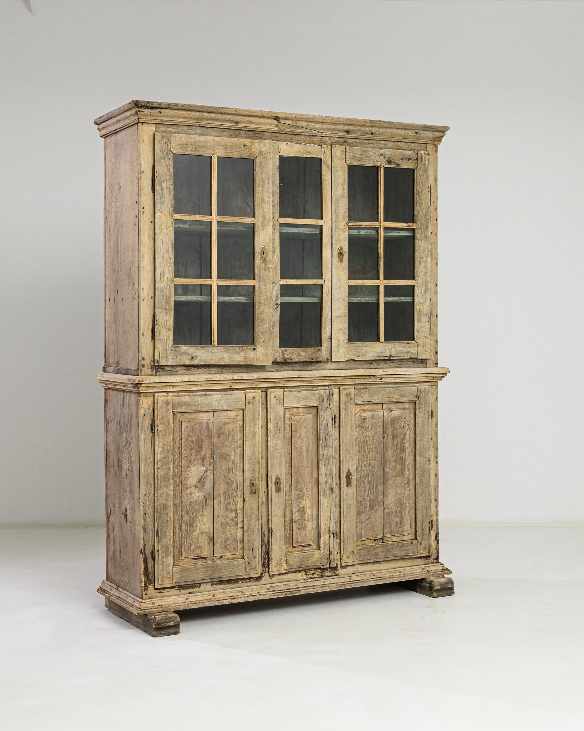 Step into the elegance of the 1840s with the German Bleached Oak Vitrine, a timeless showcase of craftsmanship. Below, three solid cabinet doors discreetly house treasures, flanked by single shelves on each side and a trio of shelves in the center.