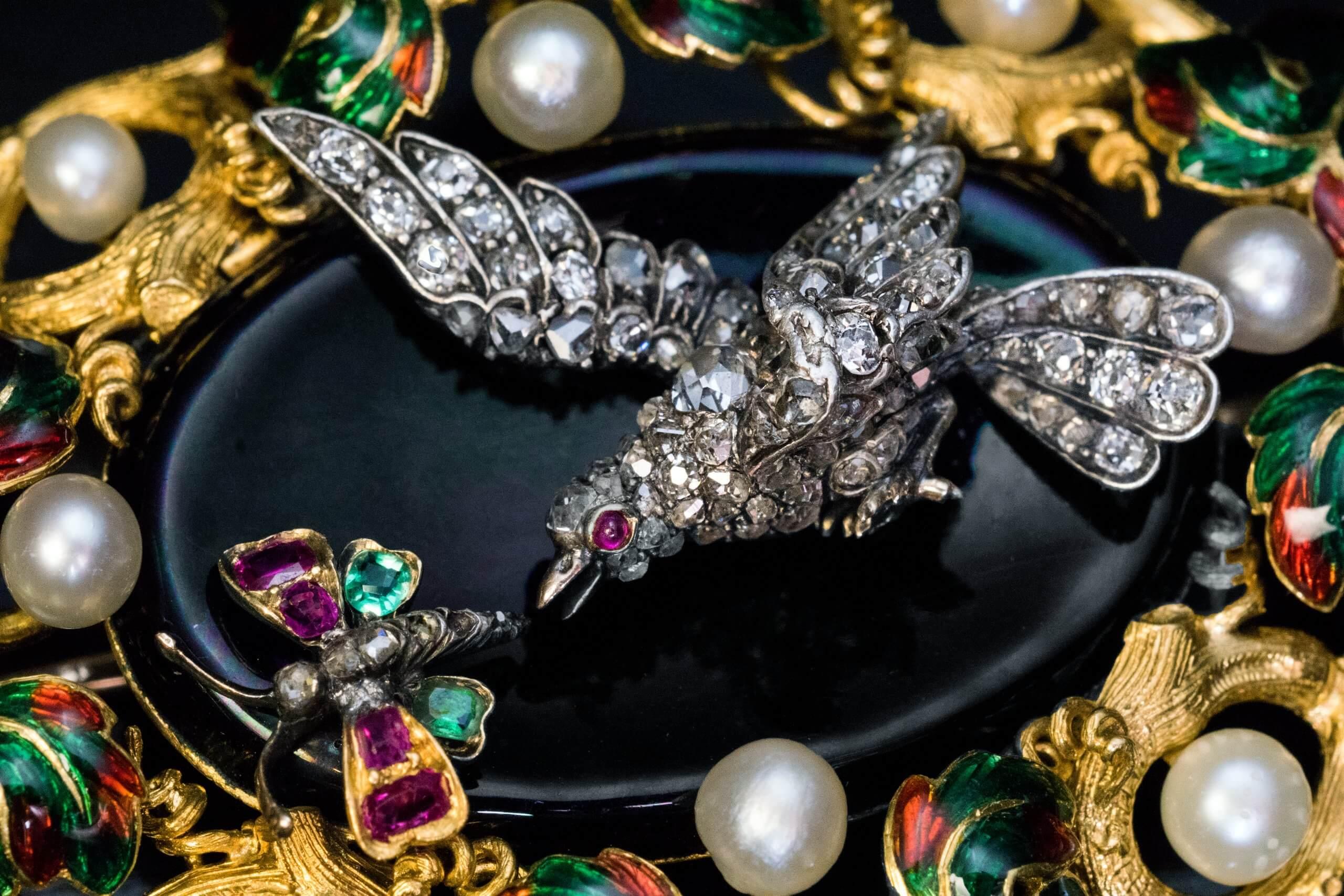Circa 1840s, most likely French.  This ornate 18K gold antique brooch is centered with a black onyx plaque depicting, a scene of a bird chasing a butterfly. The bird is superbly modeled in silver with a gold beak and eye. The body of the bird is