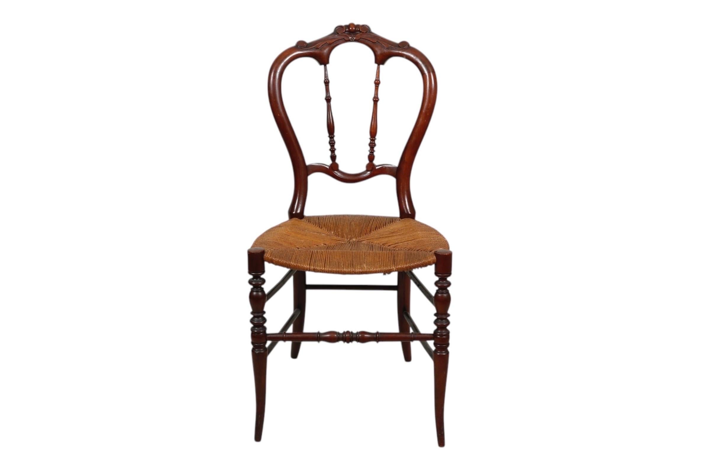 Chaise de salon victorienne en noyer, vers 1840. Le dossier en forme de tulipe est sculpté sur la traverse de la crête de simples volutes encadrées d'acanthes, soutenues par deux fuseaux tournés. L'assise en jonc tressé repose sur des pieds sabres