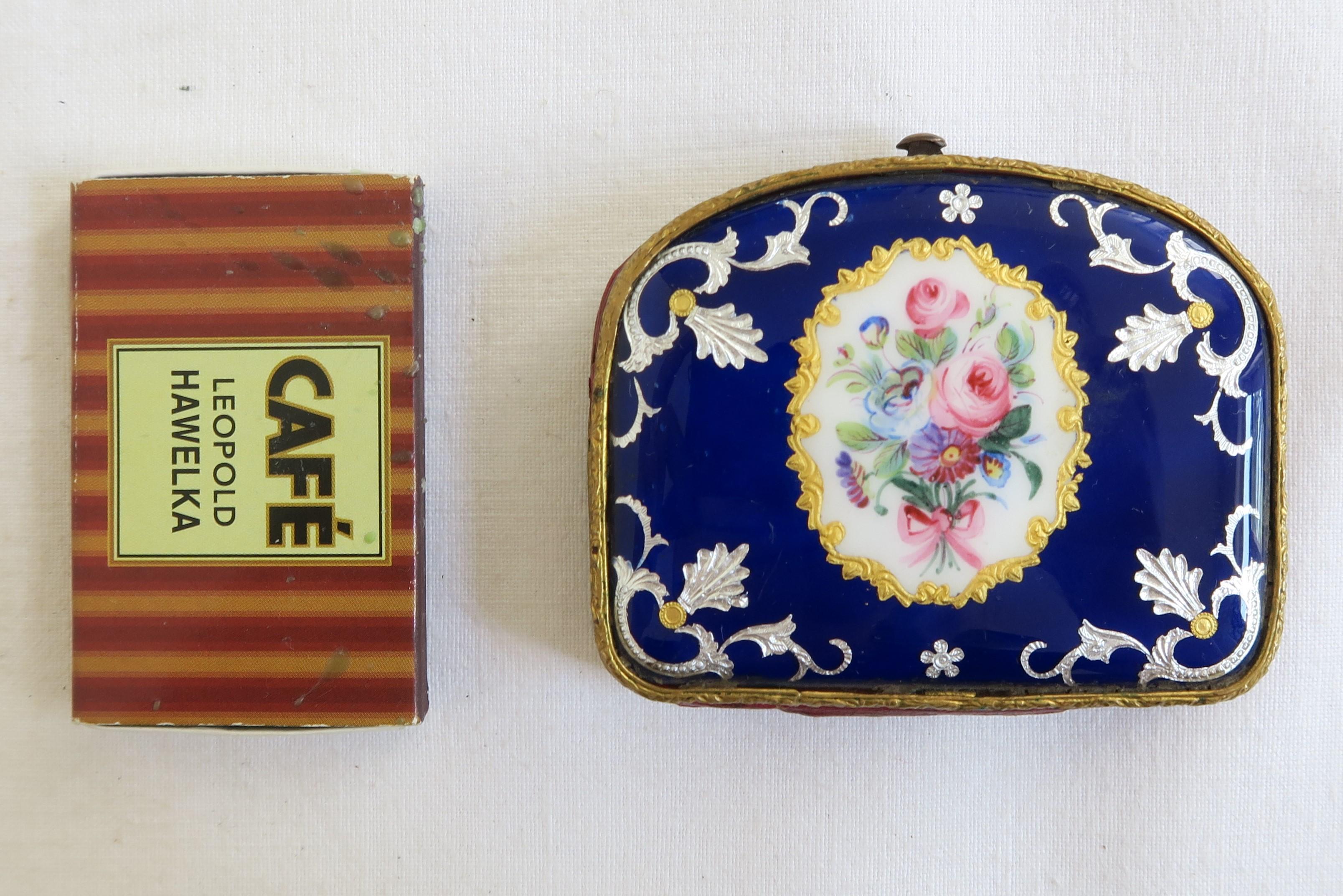 For sale is a unique little Biedermeier coin purse. Its case is made of brass covered in royal blue enamel. The lid displays an oval gold colored frame filled with white enamel with a luscious hand-painted flower bouquet in the middle. It is