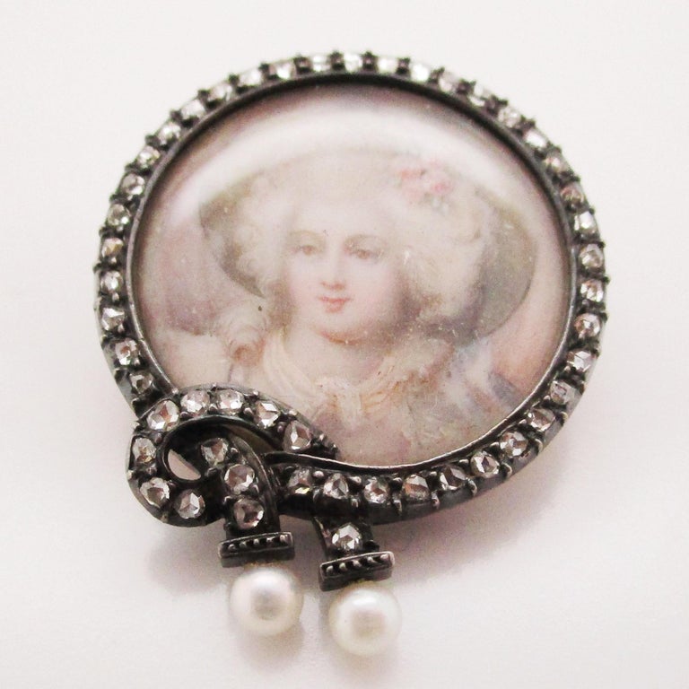 This gorgeous Victorian pin is from 1850 and features bright silver over rich 14k yellow gold and boasts a stunning hand-painted portrait nestled in a rose-cut diamond and pearl frame! The portrait is a delicately painted portrayal of a beautiful