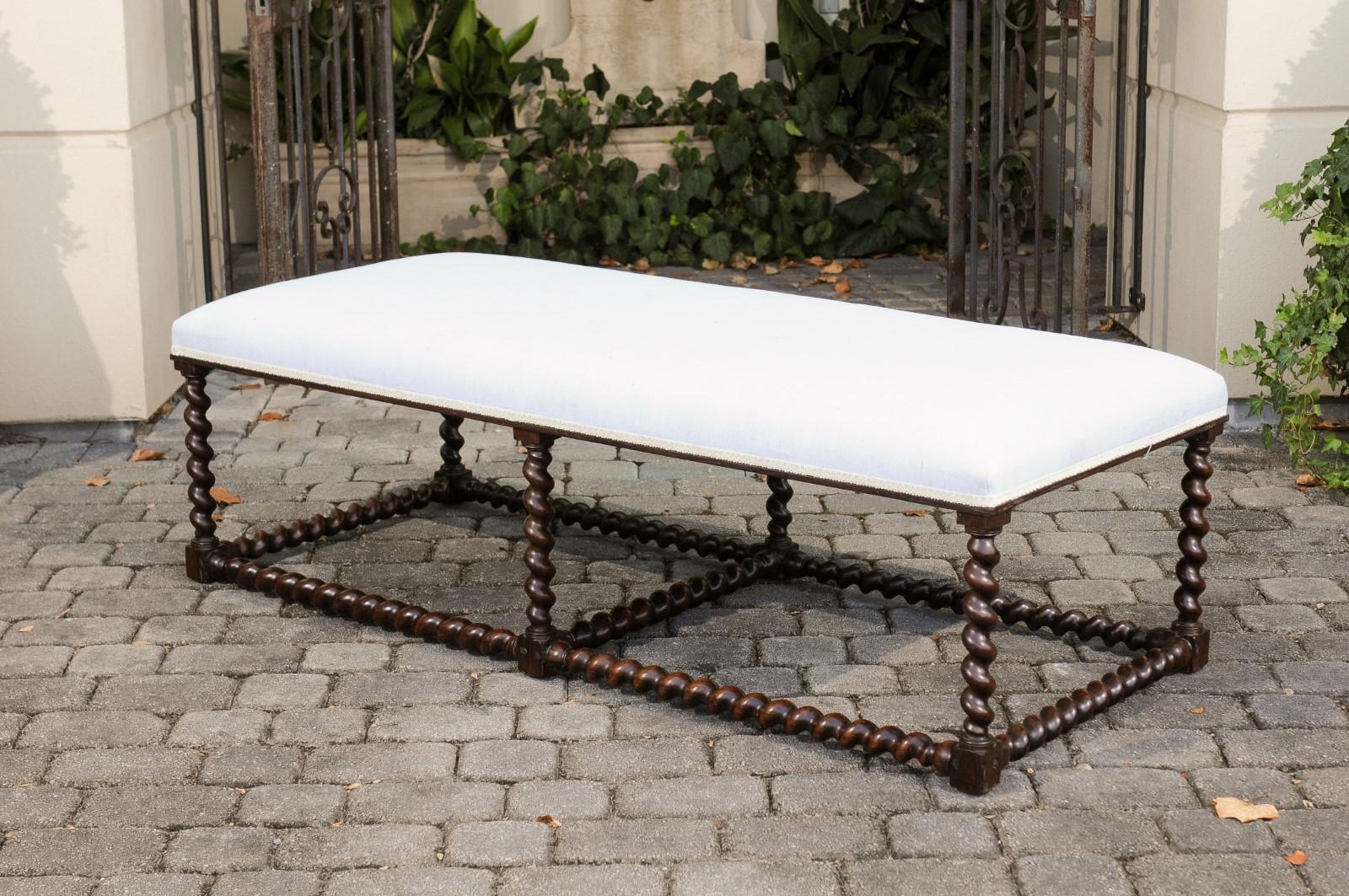 An Anglo-Indian oak bench from the mid-19th century with barley twist base and new upholstery. Born during the mid-19th century, this exquisite oak bench features a rectangular seat newly recovered with a simple muslin fabric. It is the base however