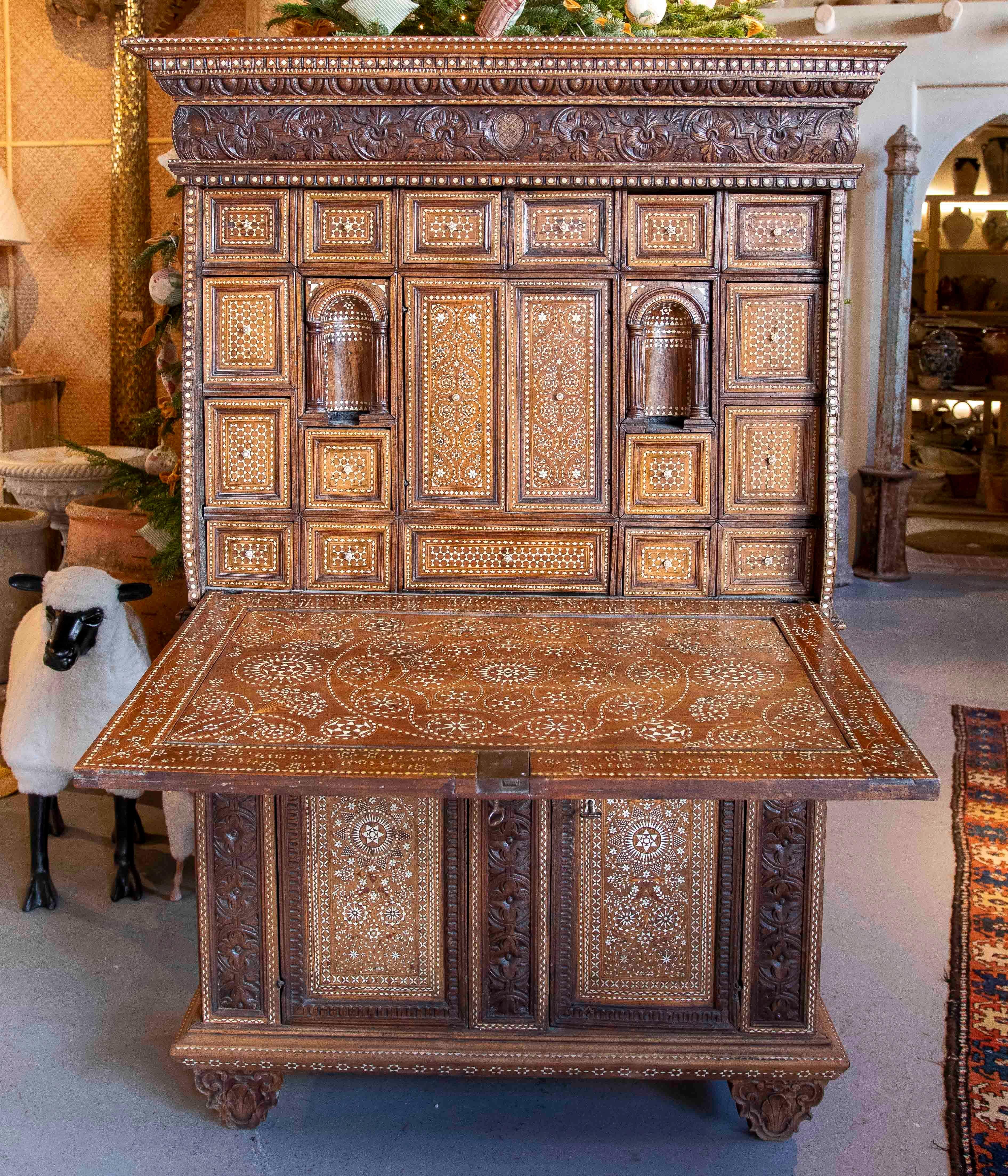 Exquisito mueble antiguo con detallada ornamentación resaltada por incrustaciones de hueso en motivos geométricos y florales. La parte frontal presenta un diseño central que evoca un árbol de la vida, rodeado de motivos de estrellas y detalles