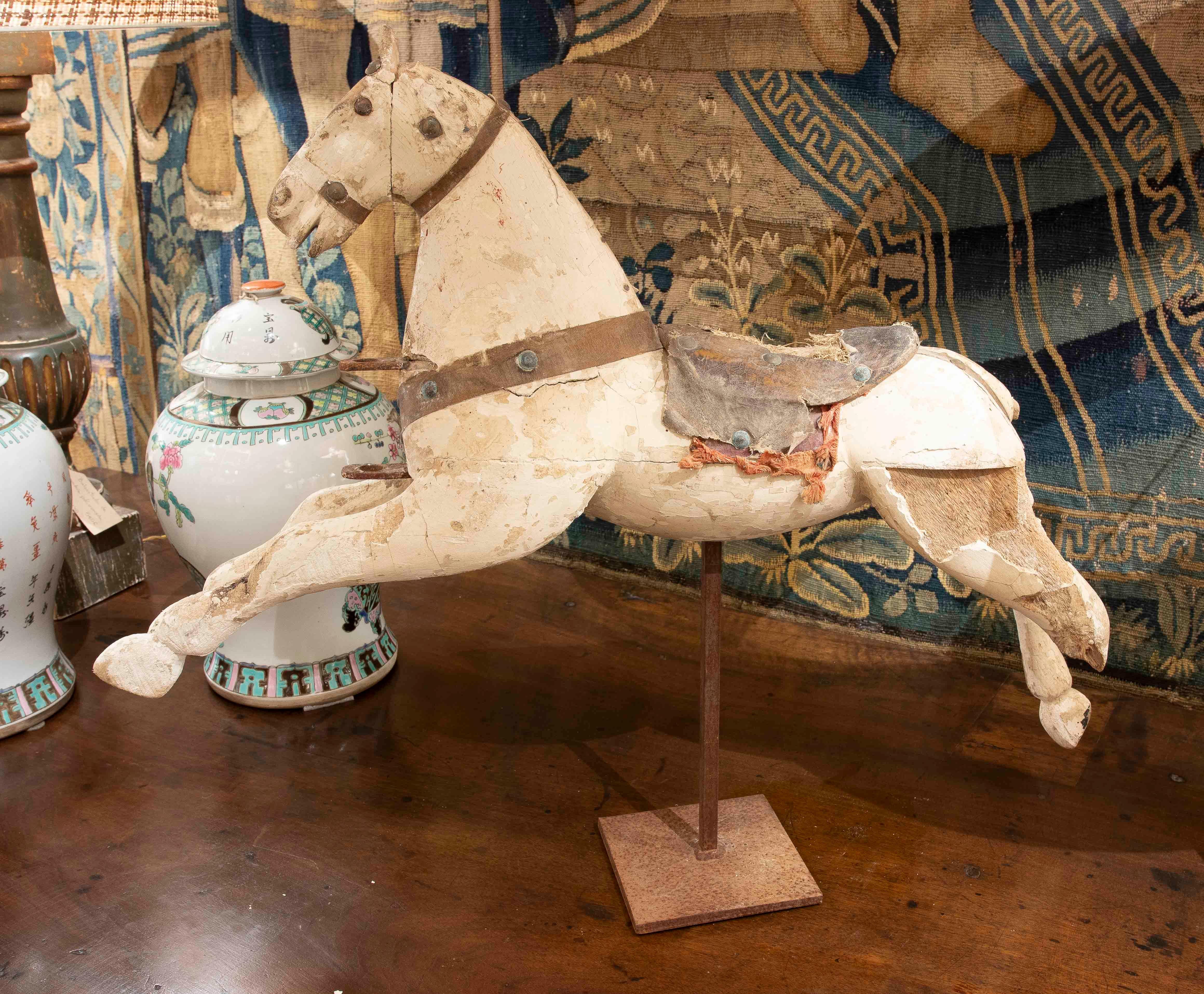 Charming vintage carved wooden rocking horse figurine with traces of original polychrome and attractive wear that accentuates its nostalgic character. It features a metal display base and retains its harness and saddle with textile details. An ideal