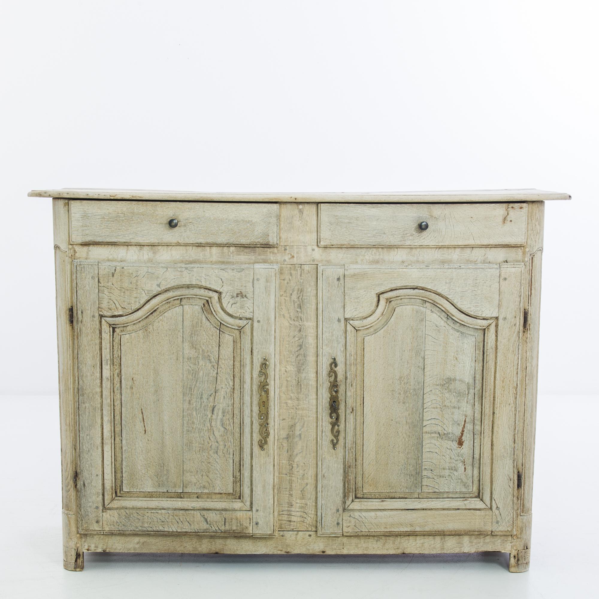 An oak buffet from Belgium, circa 1850. The upright frame is subtly embellished by the expressive swell of the paneling on the cupboard doors and the filigree of the gilded lock pieces. The wood has been restored in our workshops to a pale, natural
