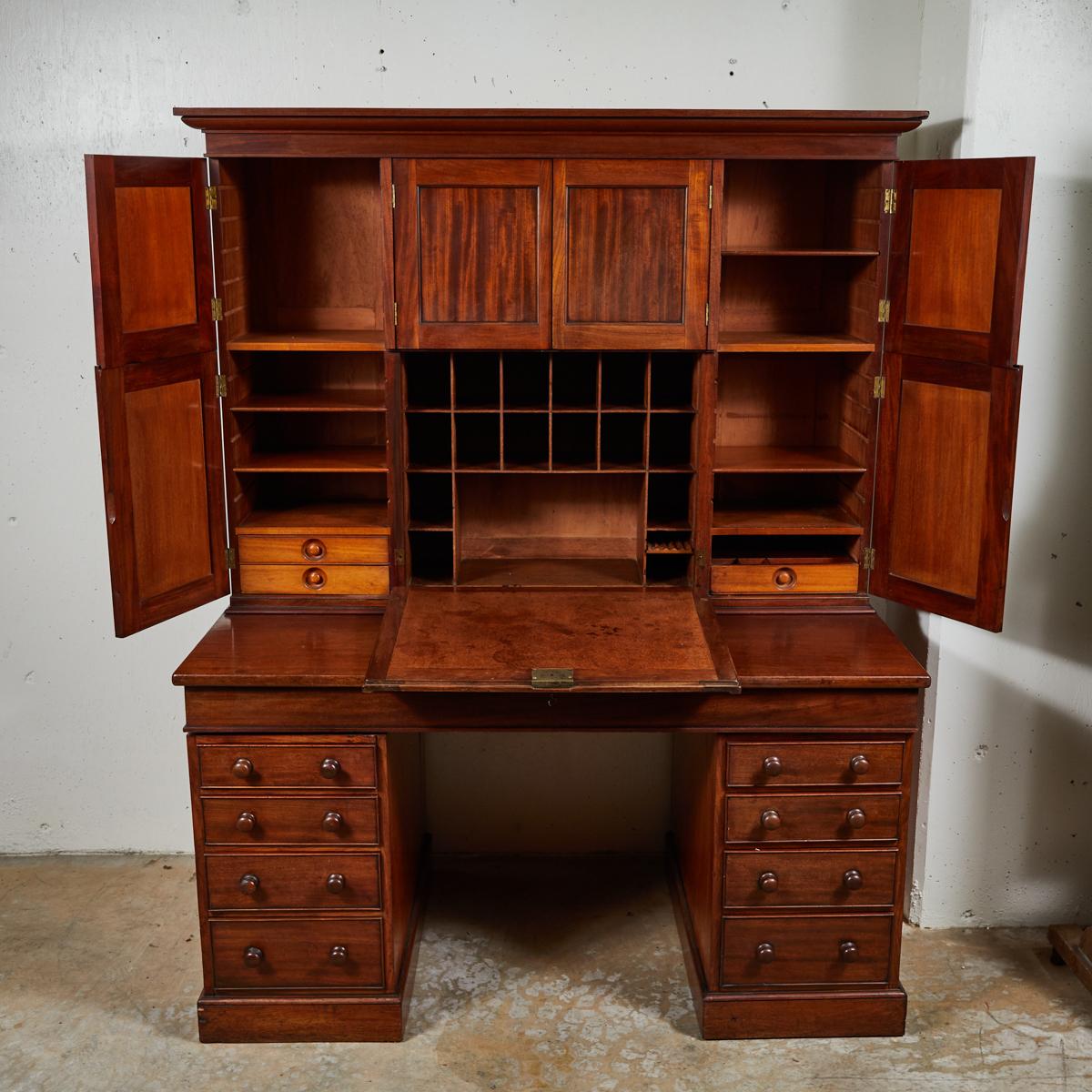 English 1850s mahogany estate desk. An exceptionally handsome piece, the upper cupboard is crowned with a simple molded cornice, and encloses a geometric array of pigeon holes, drawers and shelves. It sits mounted on a fall-front writing surface and