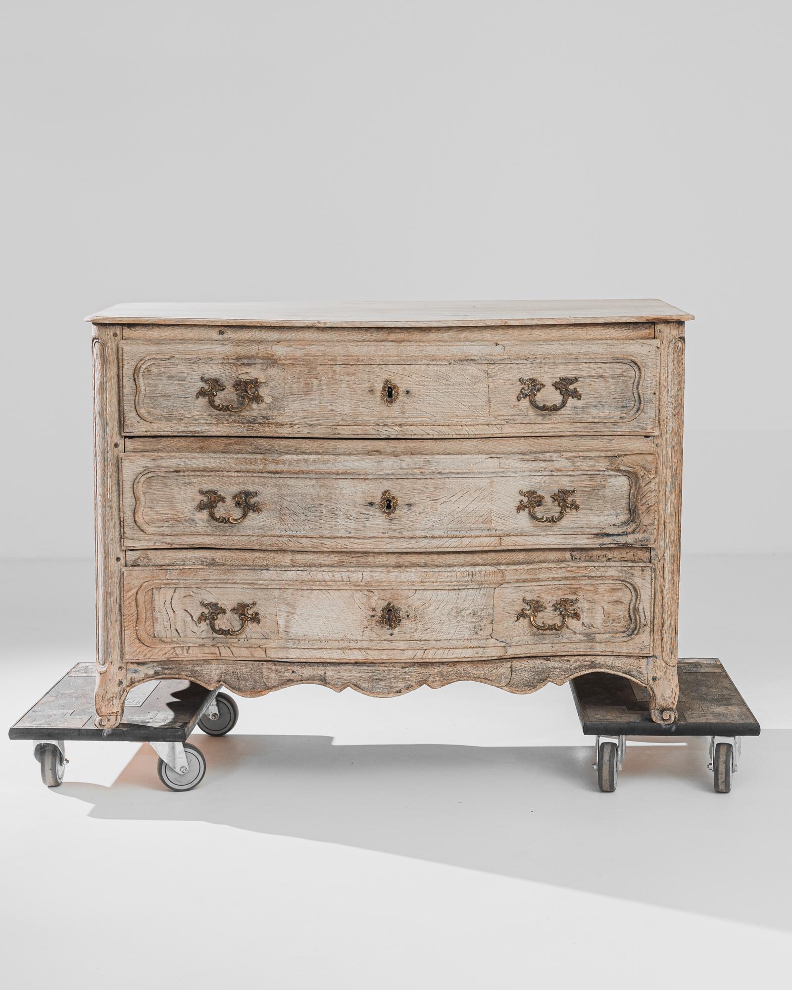 A bleached oak chest of drawers from France, produced circa 1850. This elegant antique buffet features three broad sliding drawers with brass pulls and escutcheons standing on four short feet with scroll details curling at the toes. The slight