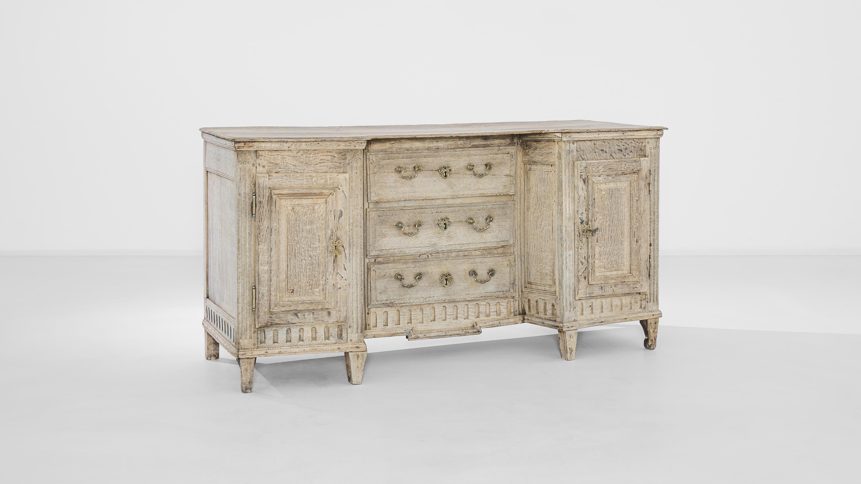 Crafted in France circa 1850, this oak cabinet features three compartments with an inset bank of drawers, giving a cozy niche to sit. The tapered feet, carved apron and fluted sides punctuate the unconventional geometry of its silhouette. Ornate
