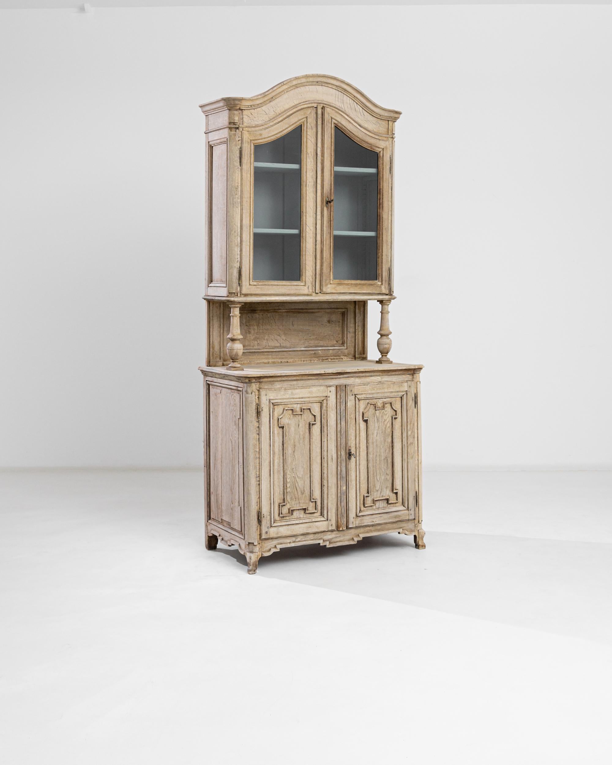 Explore the refined beauty of this 1850s French Bleached Oak Vitrine, an exquisite blend of elegance and country simplicity. Crafted in France during the 1800s, the graceful arch of the cornice harmoniously mirrors the lower cupboard doors, creating