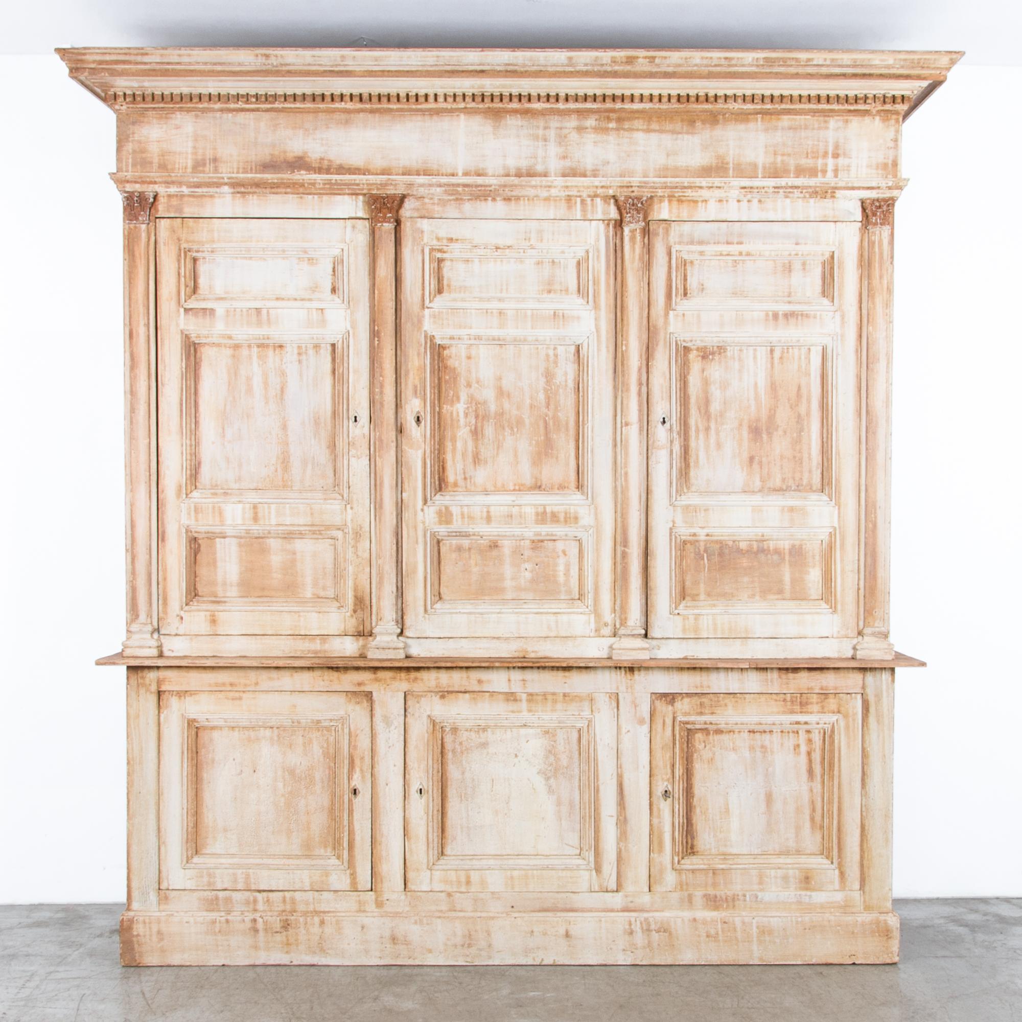 A wooden cabinet from France, circa 1850s, featuring three hinged doors which open onto two interior shelves. On an impressive scale, the neoclassical influence is enhanced by the distinctive mottled patina, while the interior has been repainted in